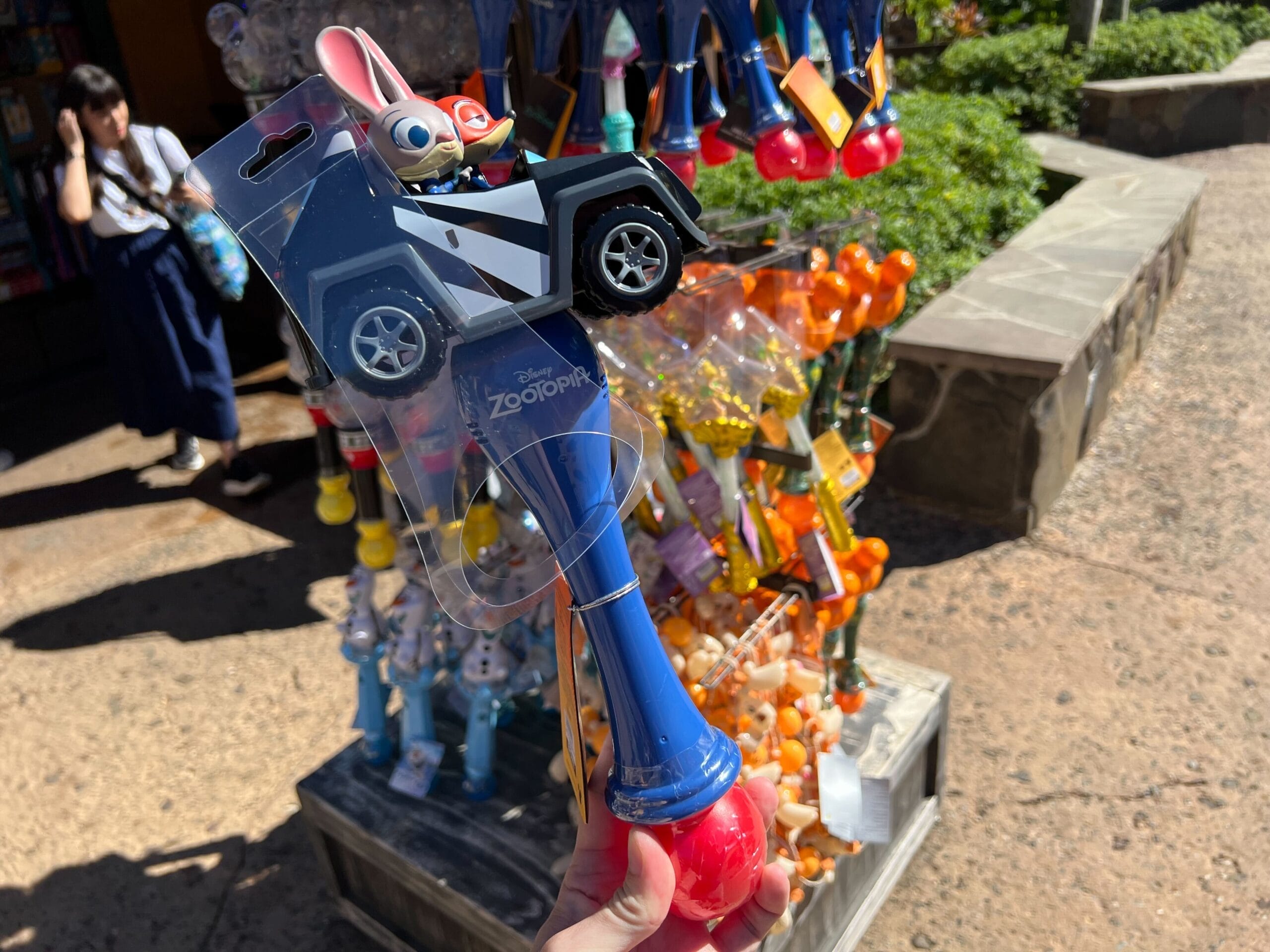 A hand holds a blue and red Zootopia Judy Hopps toy wand, showcased in today’s recap of colorful Disney Park toys.