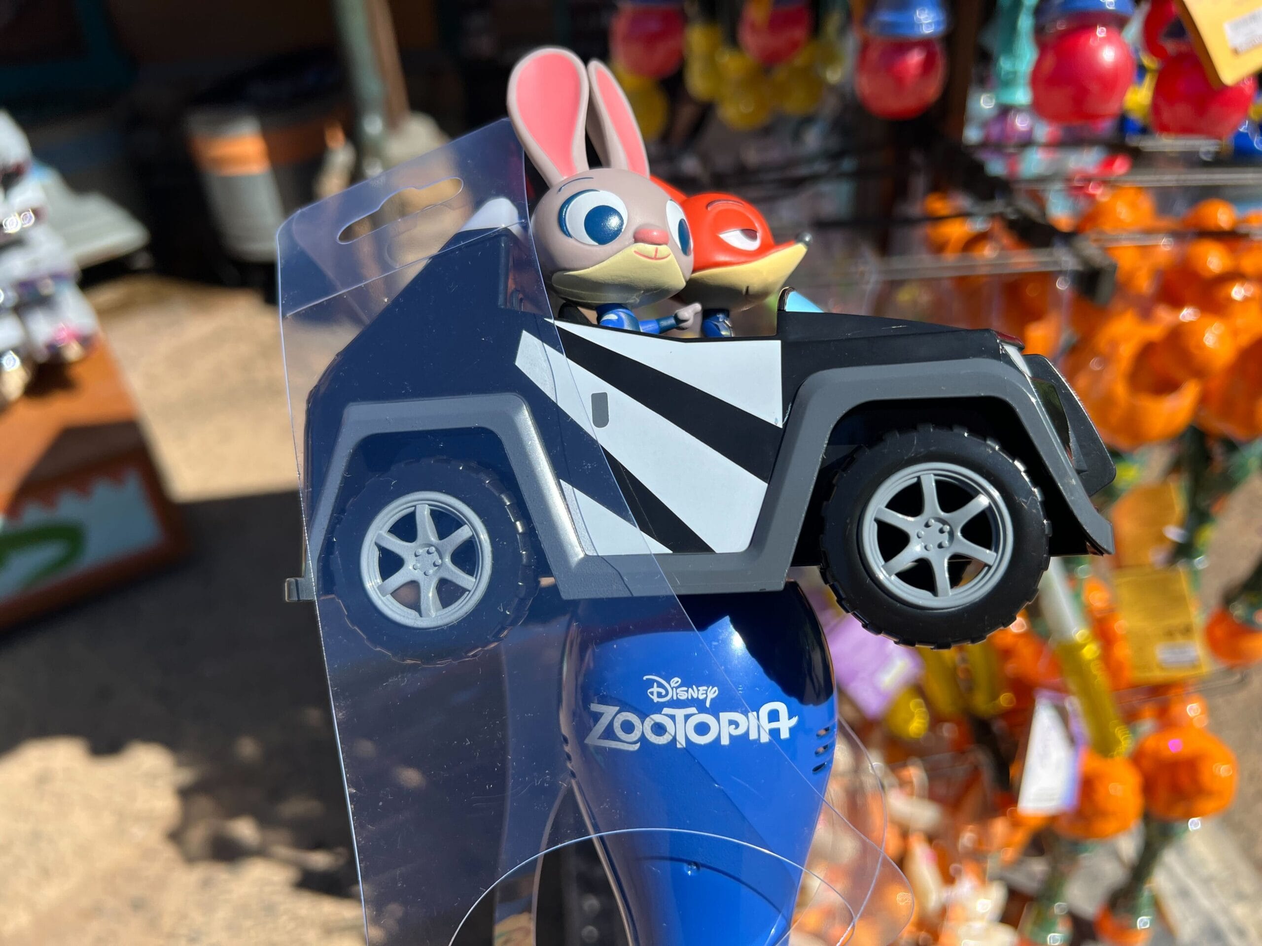 Zootopia toy car with Judy Hopps and Nick Wilde on a Disney park shop display, colorful merchandise in the background.