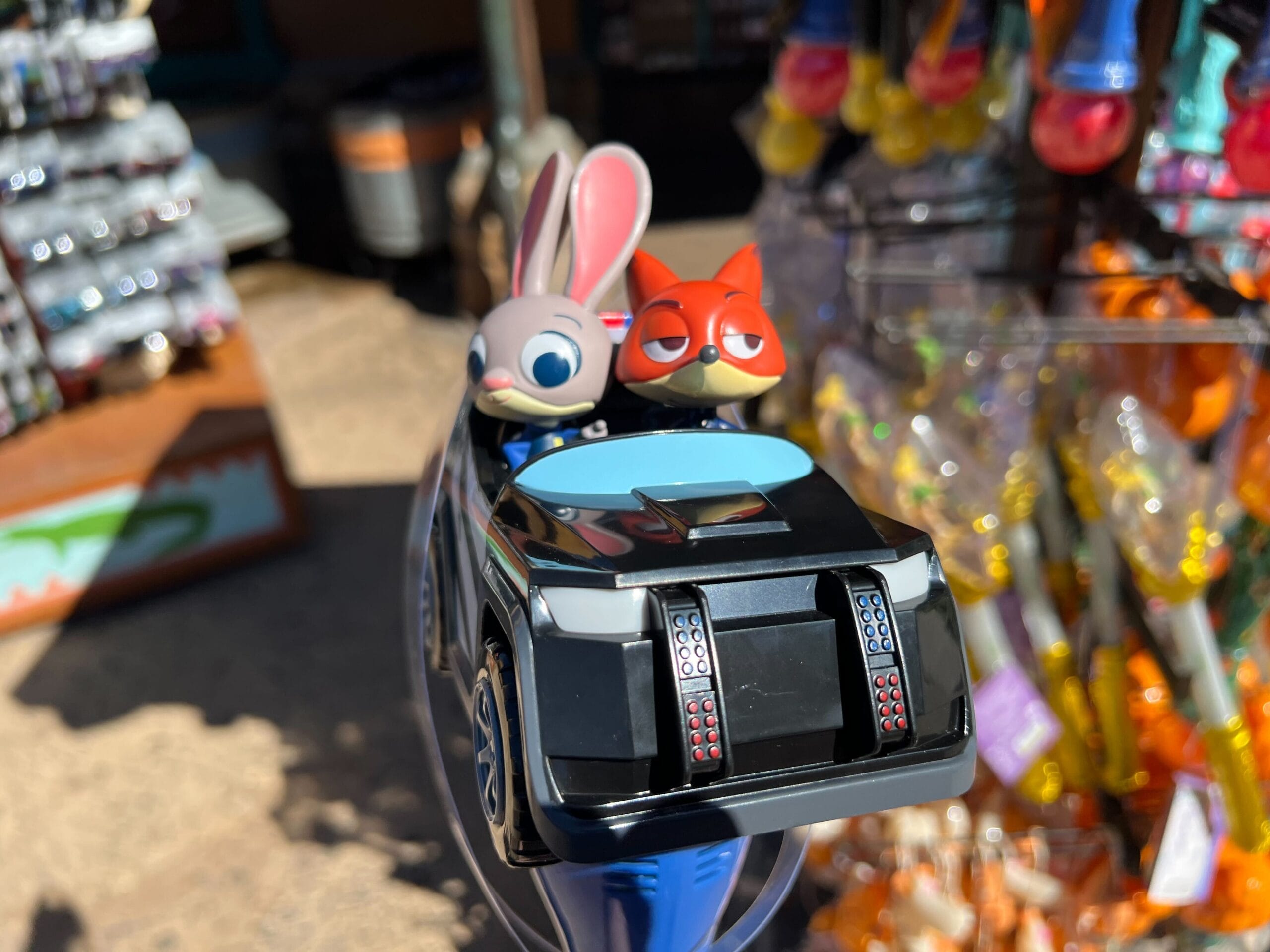 Zootopia bunny and fox toy car among colorful Disney Park keychains and trinkets, reminiscent of park souvenir displays.