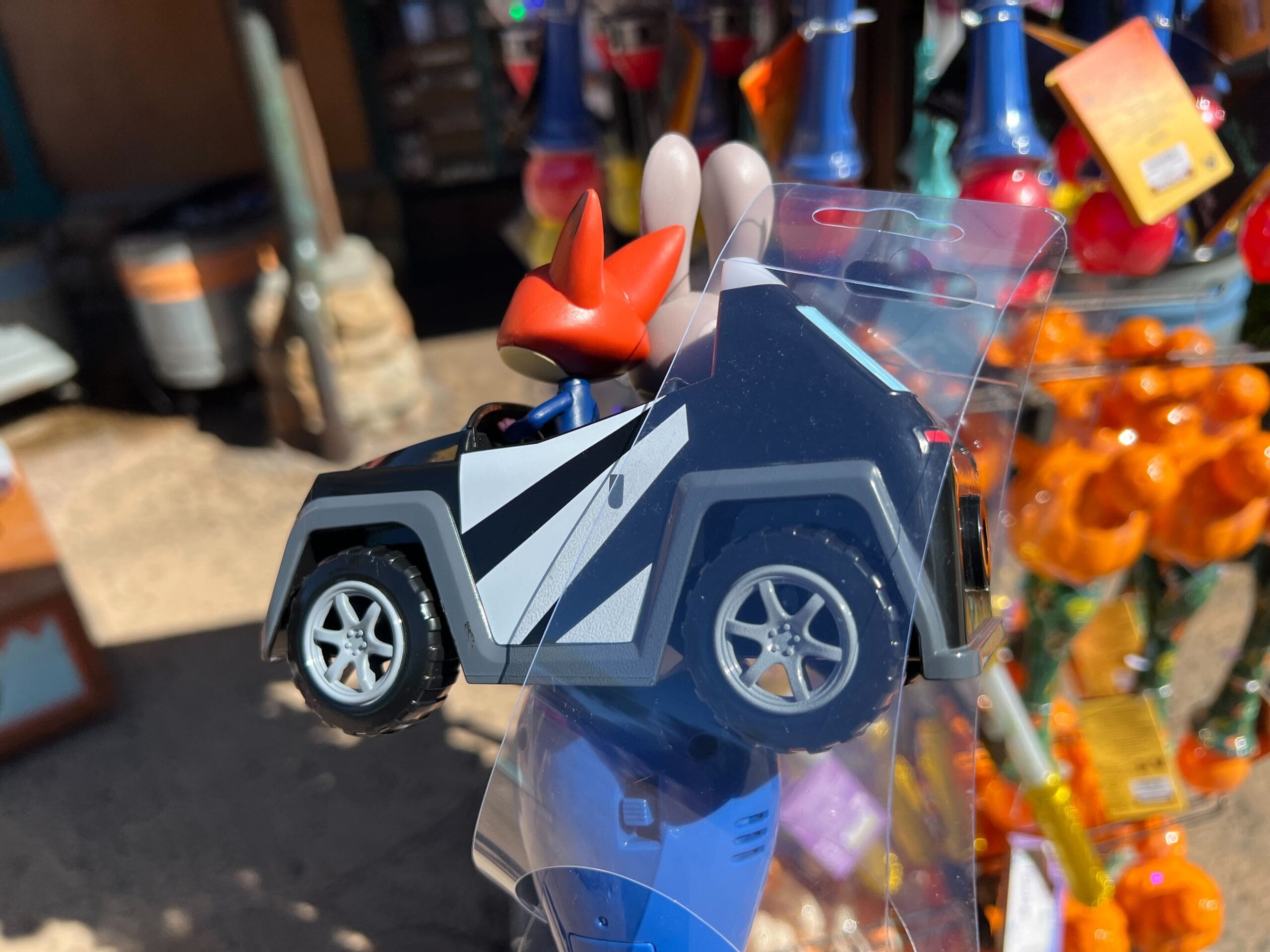A toy fox character sits in a small blue-and-white toy car on display in a store, reminiscent of Disney park merchandise.