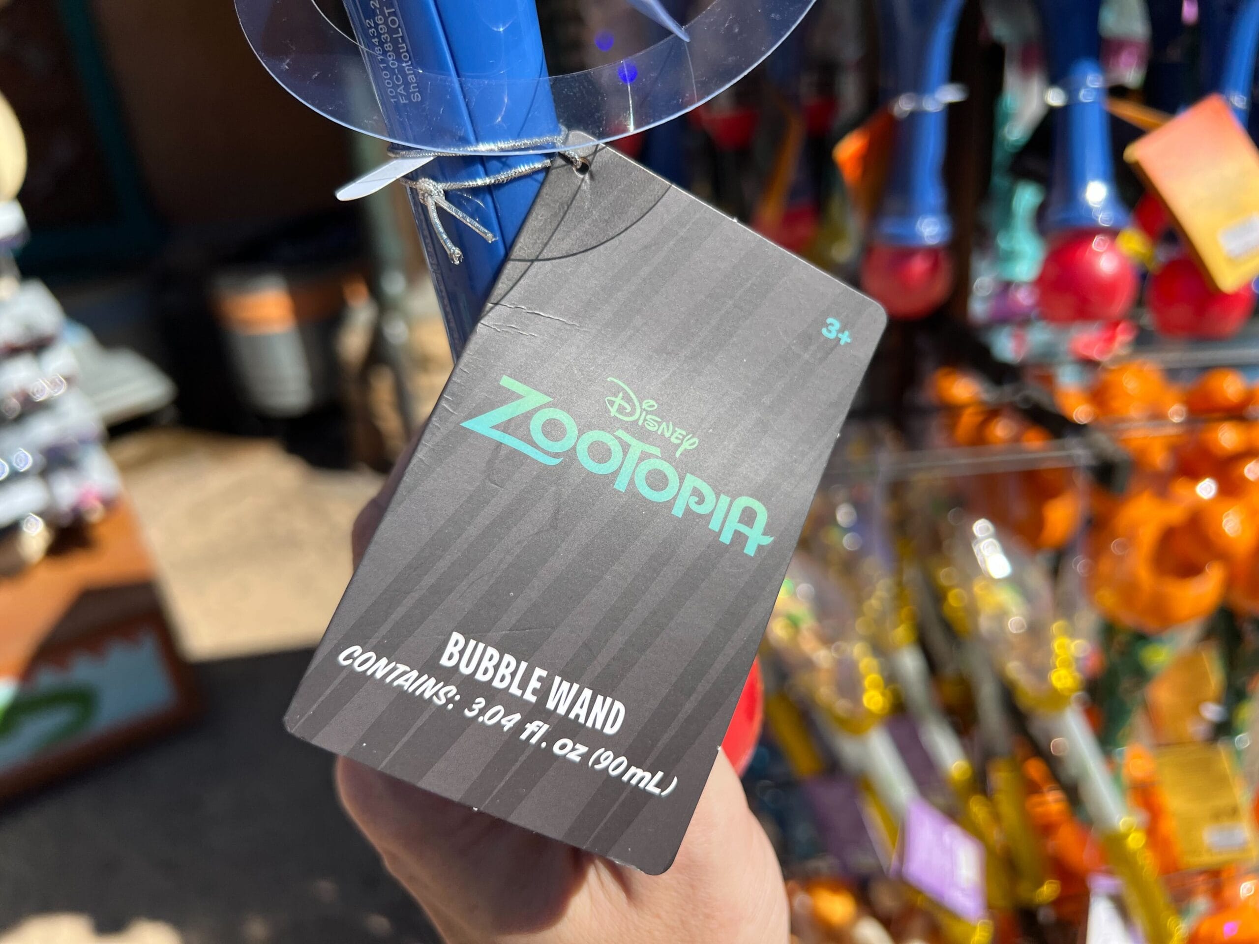 A Zootopia bubble wand tag showing 3.04 fl. oz. (90 ml), held outside near toys—no Disney castle like those in the parks visible.