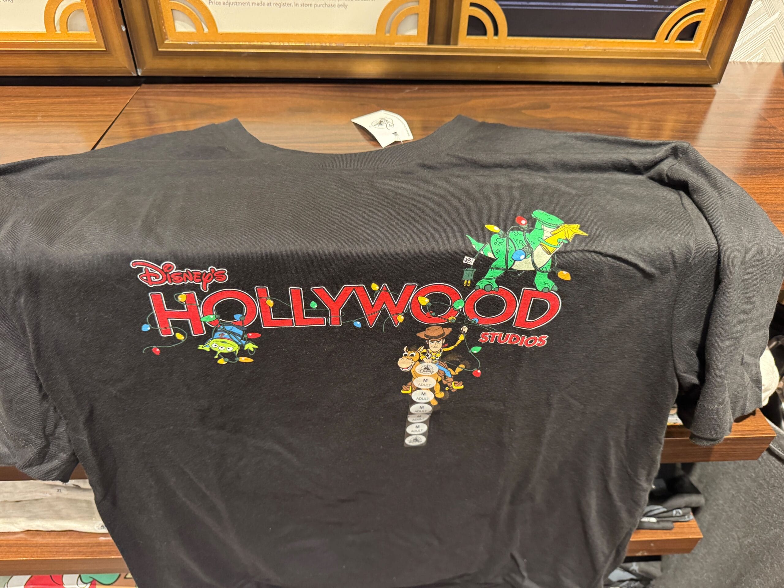 Black t-shirt featuring Disney’s Hollywood Studios logo and Toy Story characters wrapped in Christmas lights, no castle shown.