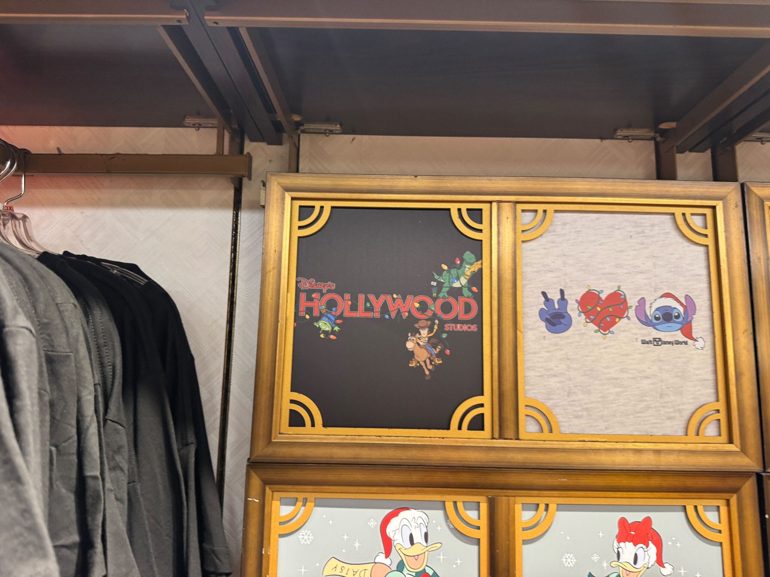 Shirts on display feature a Disney’s Hollywood Studios design with Mickey, Minnie, Goofy, and Pluto—classic Walt Disney World icons.
