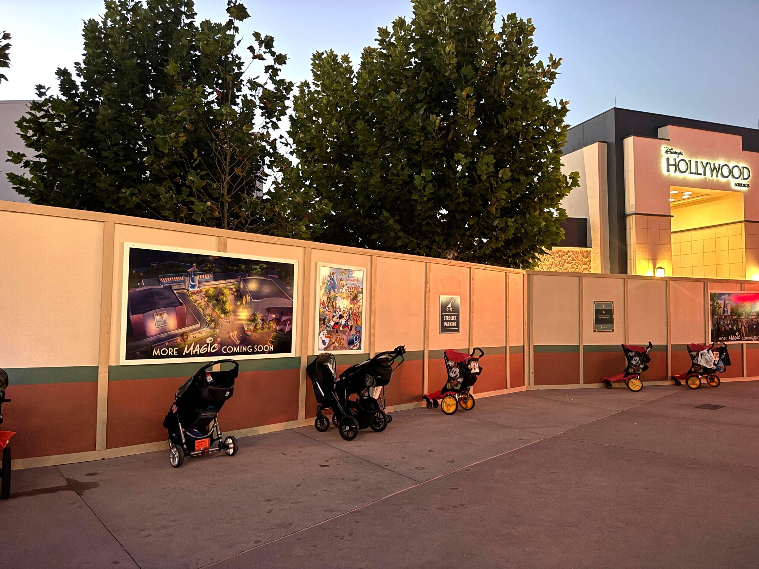 Strollers line construction walls at dusk in Disney's Hollywood Studios, near a "Hollywood" sign—no castle in view.