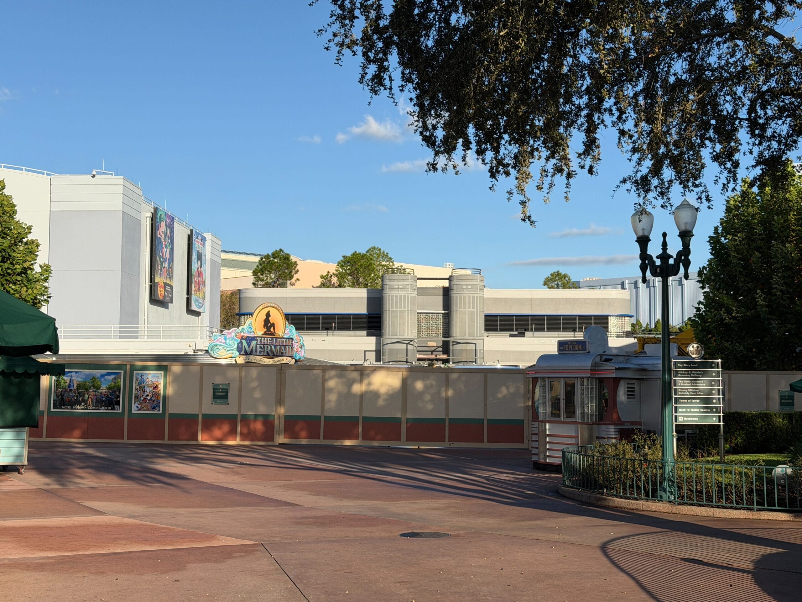 Construction walls surround The Little Mermaid ride in Animation Courtyard, no arch seen, under a blue sky at Disney's Hollywood Studios.