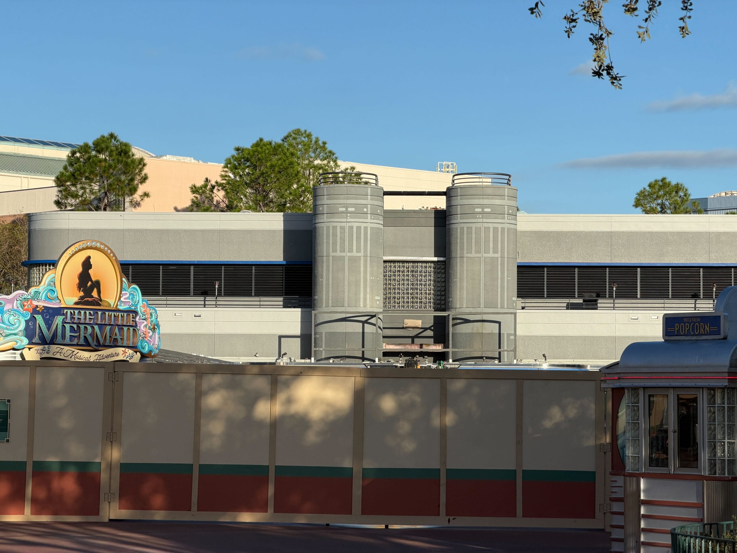 Construction walls in Animation Courtyard near "The Little Mermaid" sign; demolished arch, gray show building reminiscent of Disney parks.