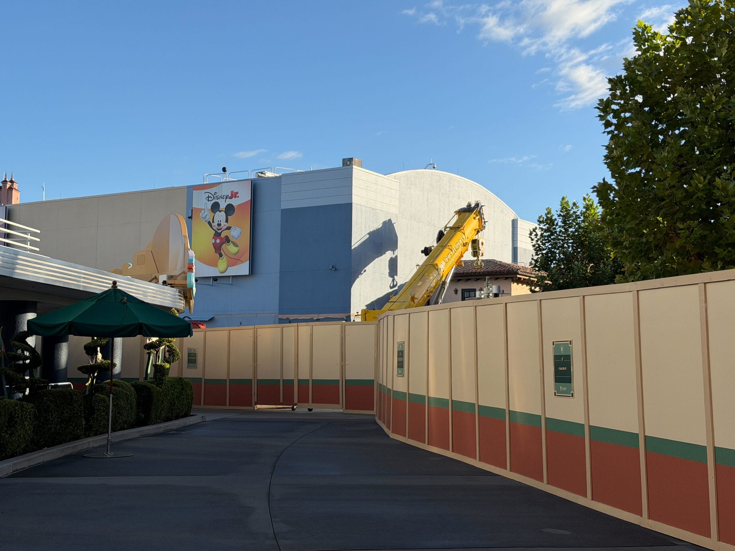 Construction zone with beige walls and a crane in Animation Courtyard by a Mickey Mouse sign, all beneath a clear blue sky at Disney.