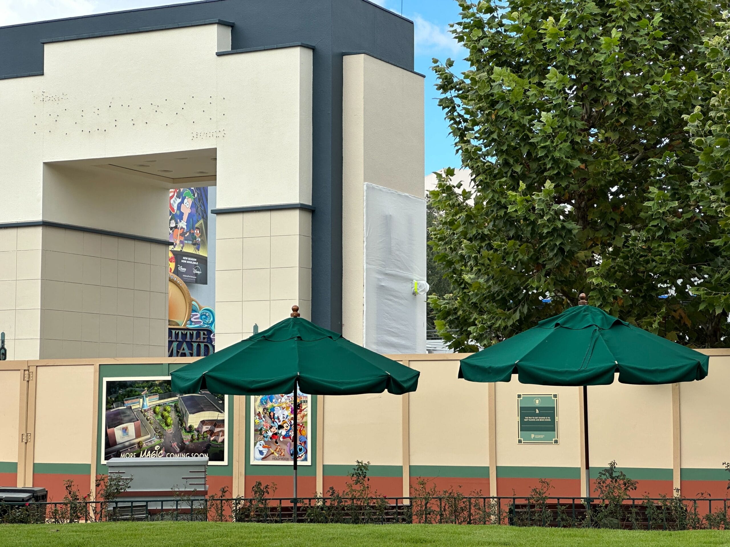 Outdoor seating with green umbrellas near a demolition wall at Disney's Hollywood Studios; buildings and trees in the background.