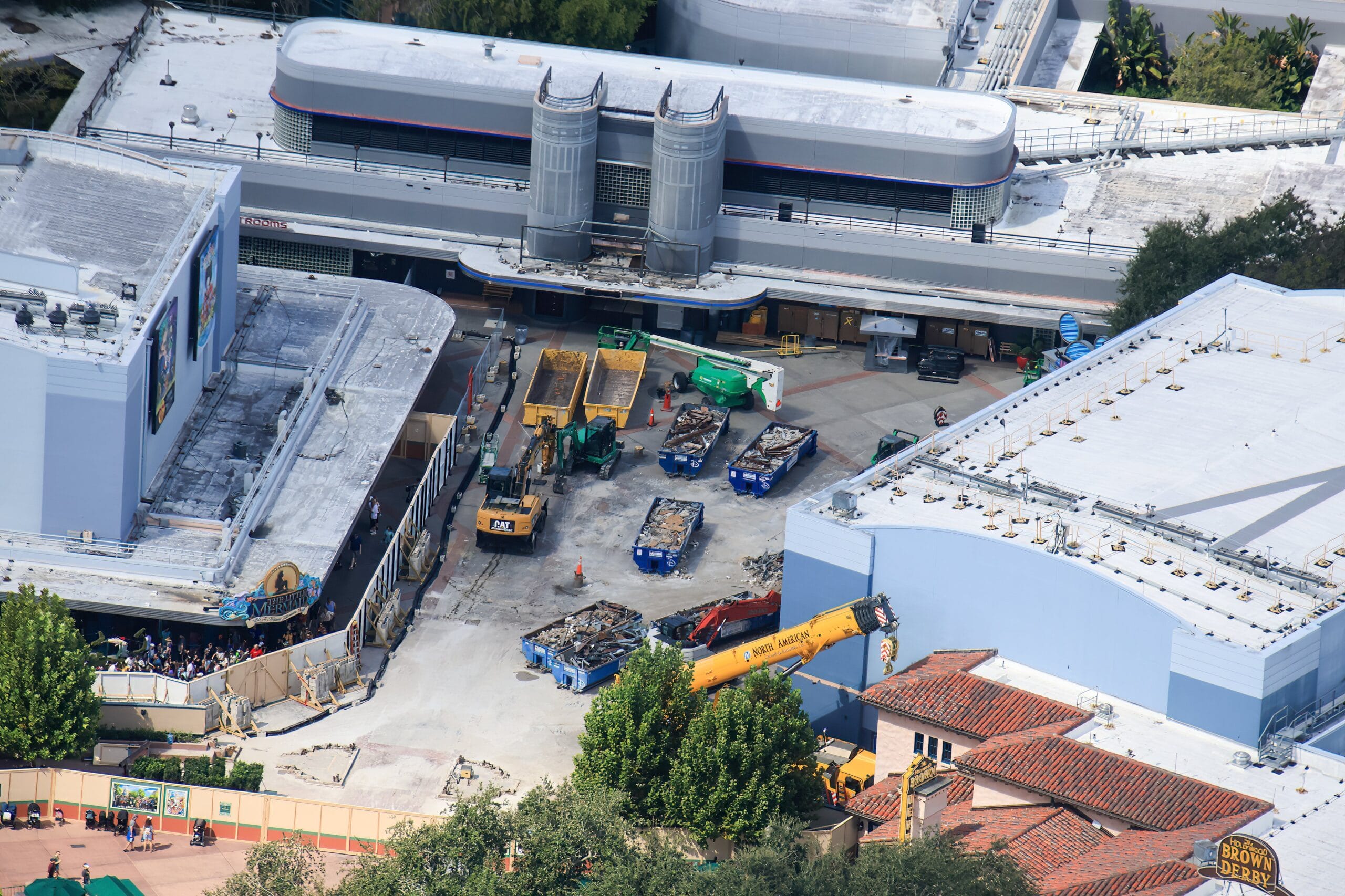 Aerial view of demolition near Animation Courtyard Arch at Disney, with dumpsters, debris, and heavy machinery by blue buildings.
