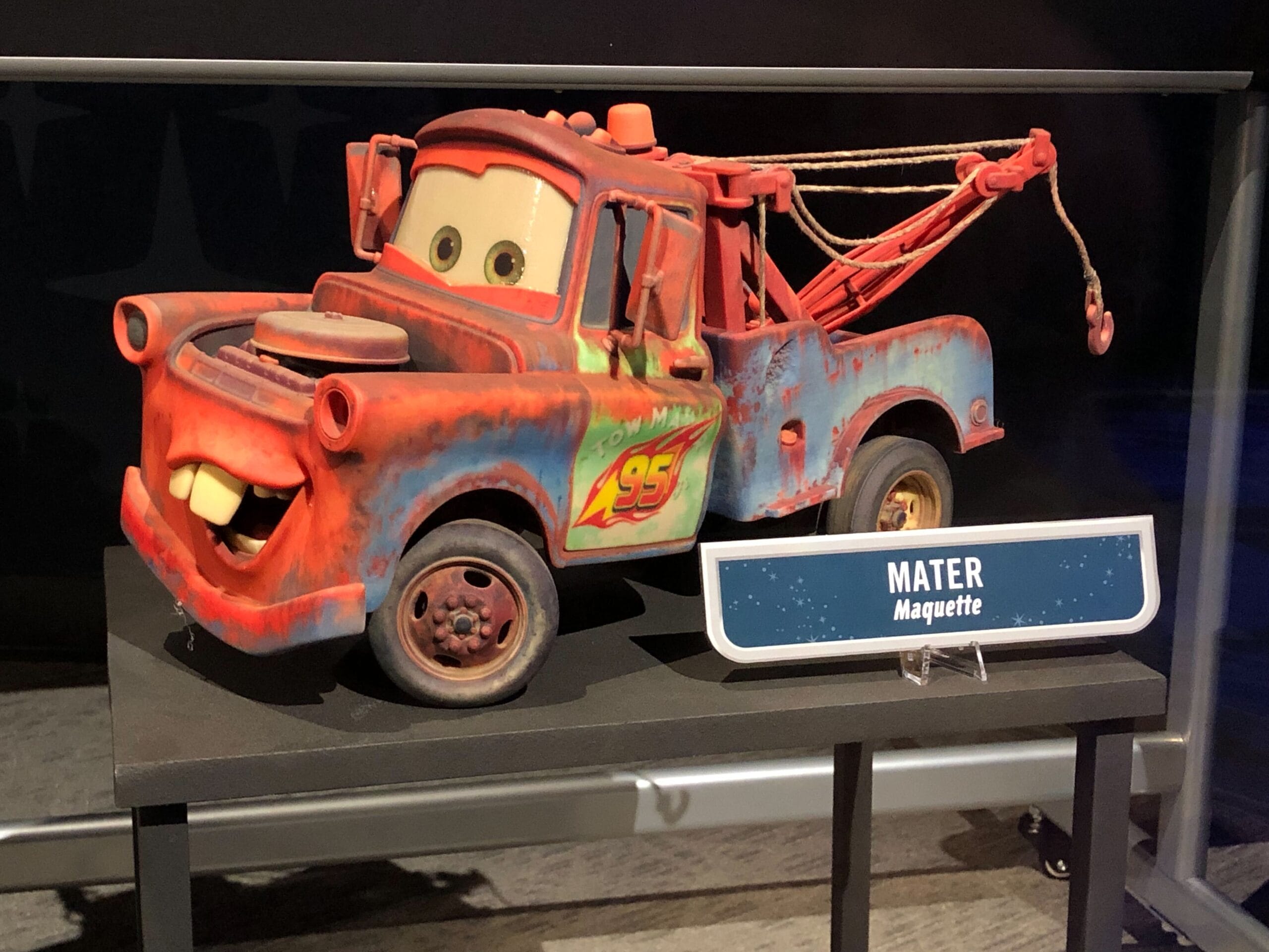 A vibrant Mater maquette with a Lightning McQueen logo stands in Cars Land, Disneyland Resort, on a base with a nameplate.
