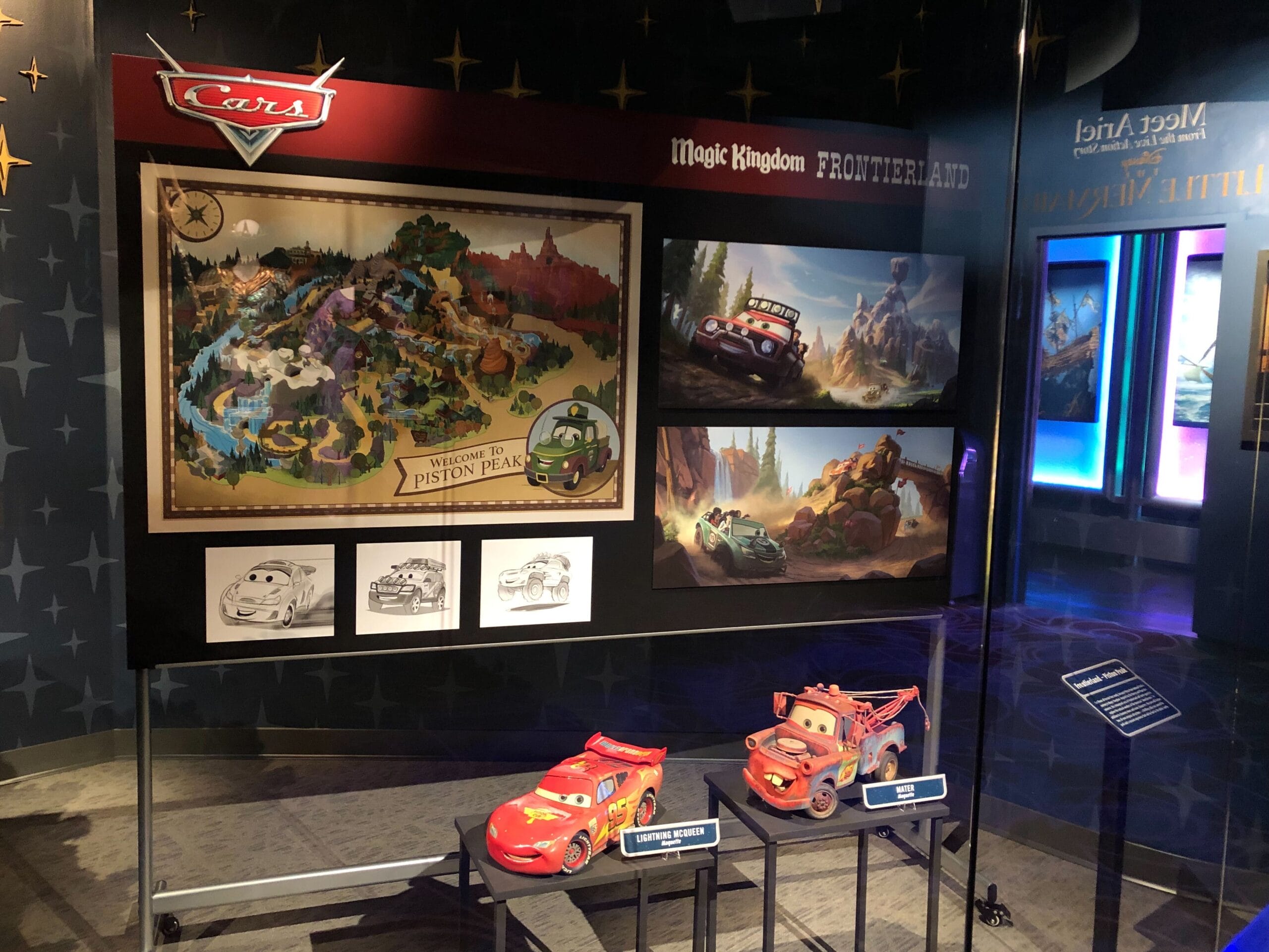 Cars Land concept art, models, and artwork from Disney Parks displayed in a glass case at a themed exhibit or museum.
