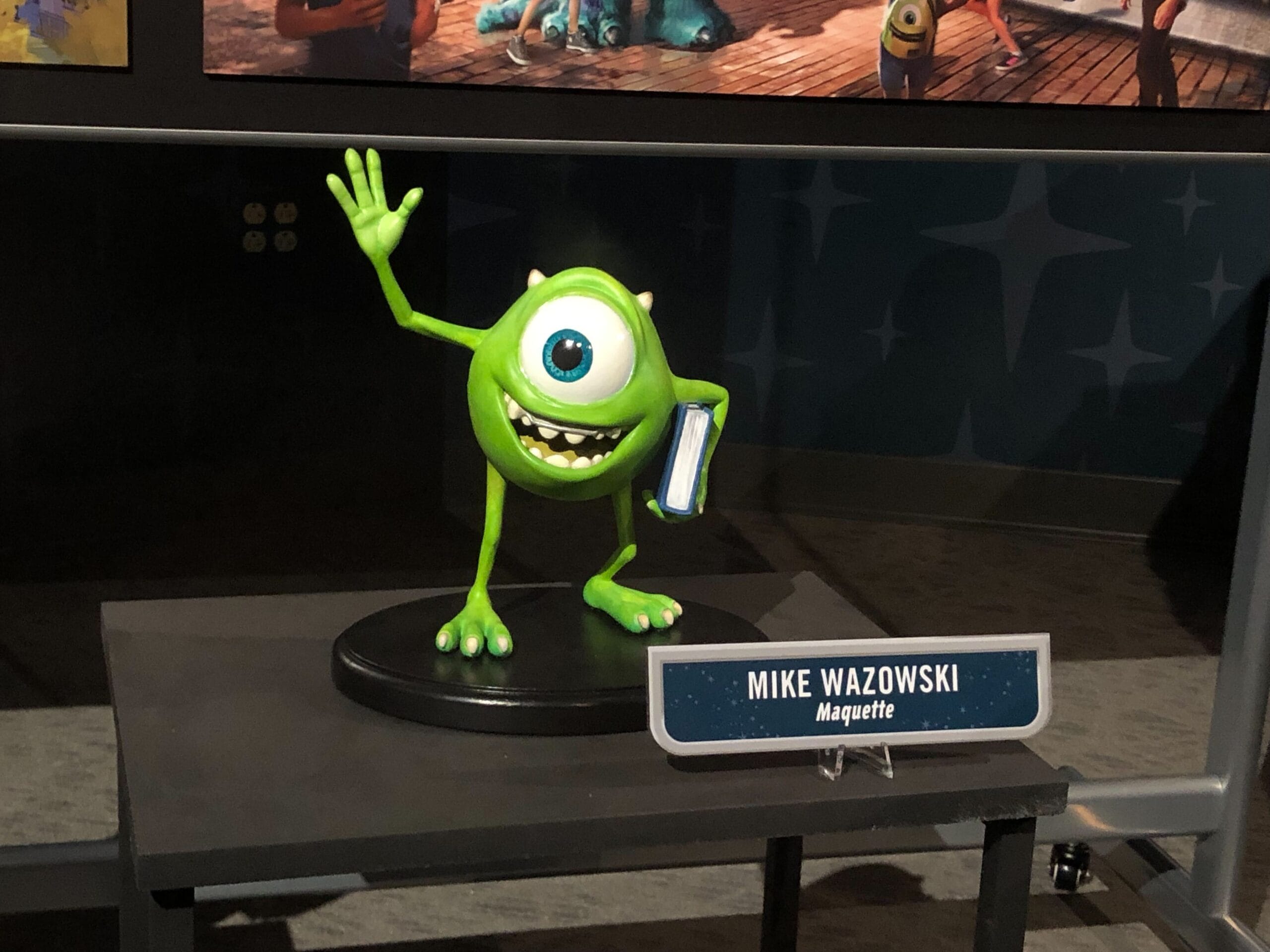 Mike Wazowski figurine on display, waving and holding a Monsters Inc. coaster, reminiscent of similar Disney Parks merchandise.