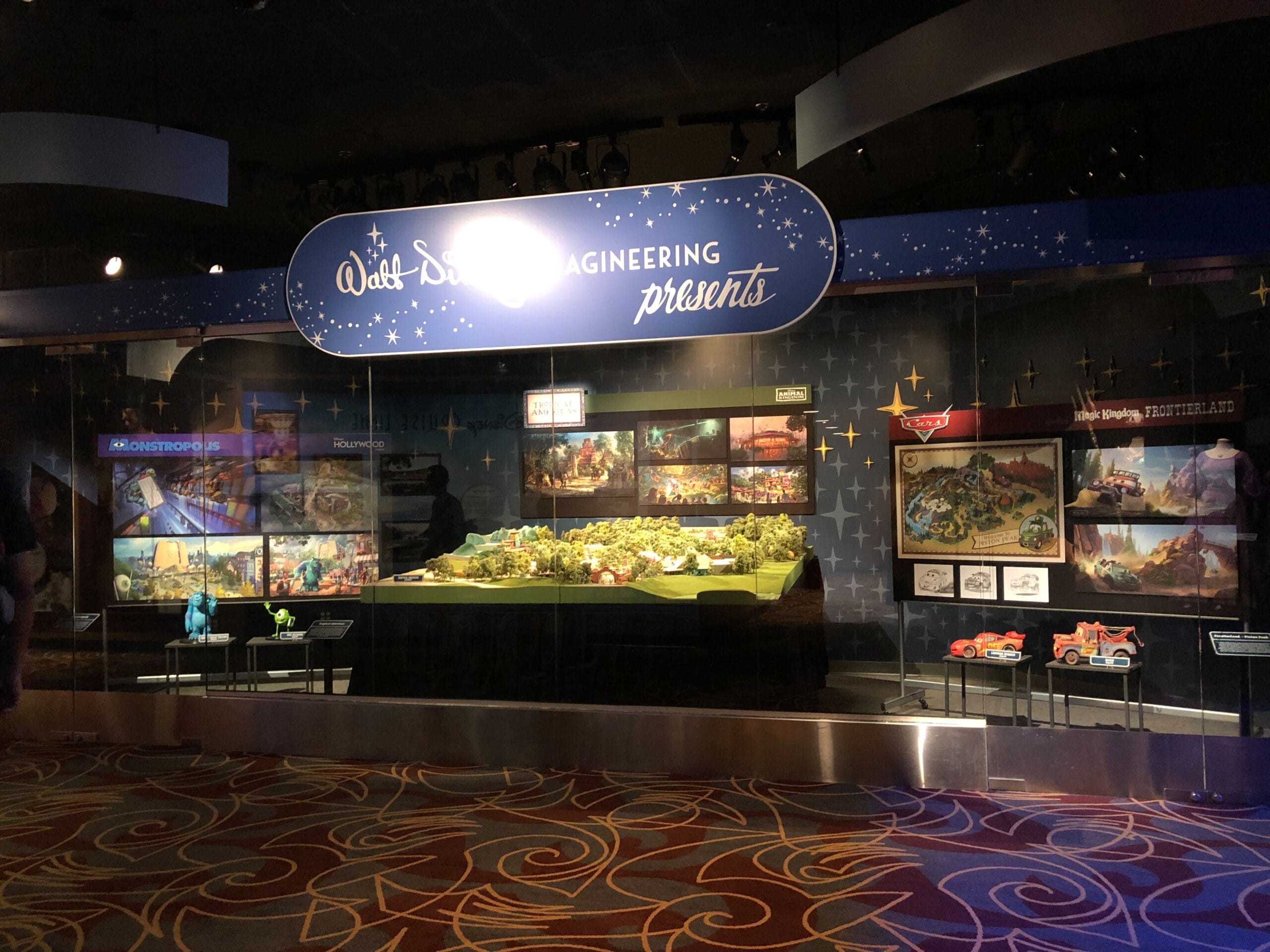 A Disney Imagineering exhibit displays Animal Kingdom and Cars Land models, with no castle present to compare to other Disney parks.