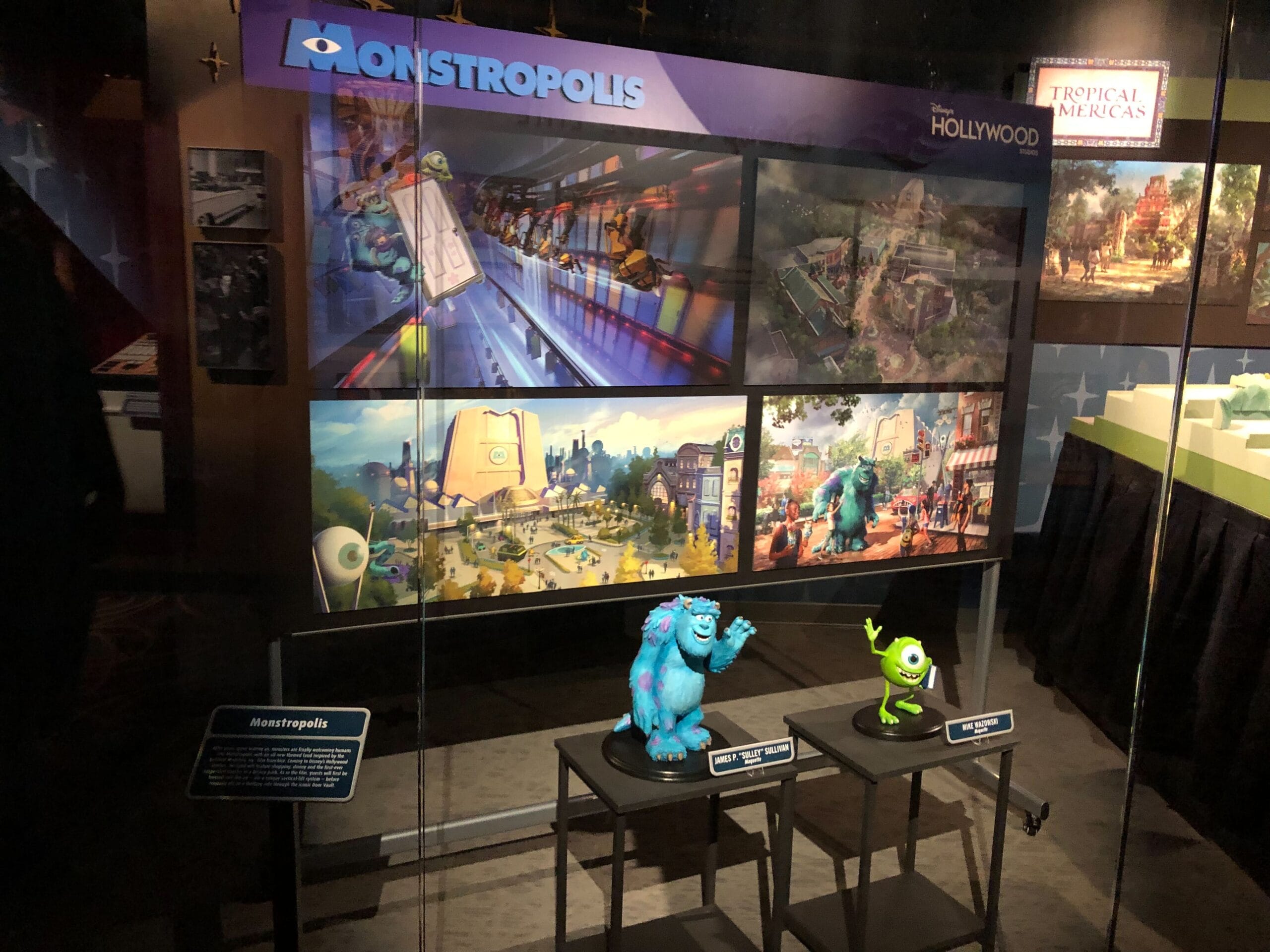 Glass case display featuring Monstropolis concept art and Sulley and Mike models from Monsters Inc. Coaster at a Disney park.