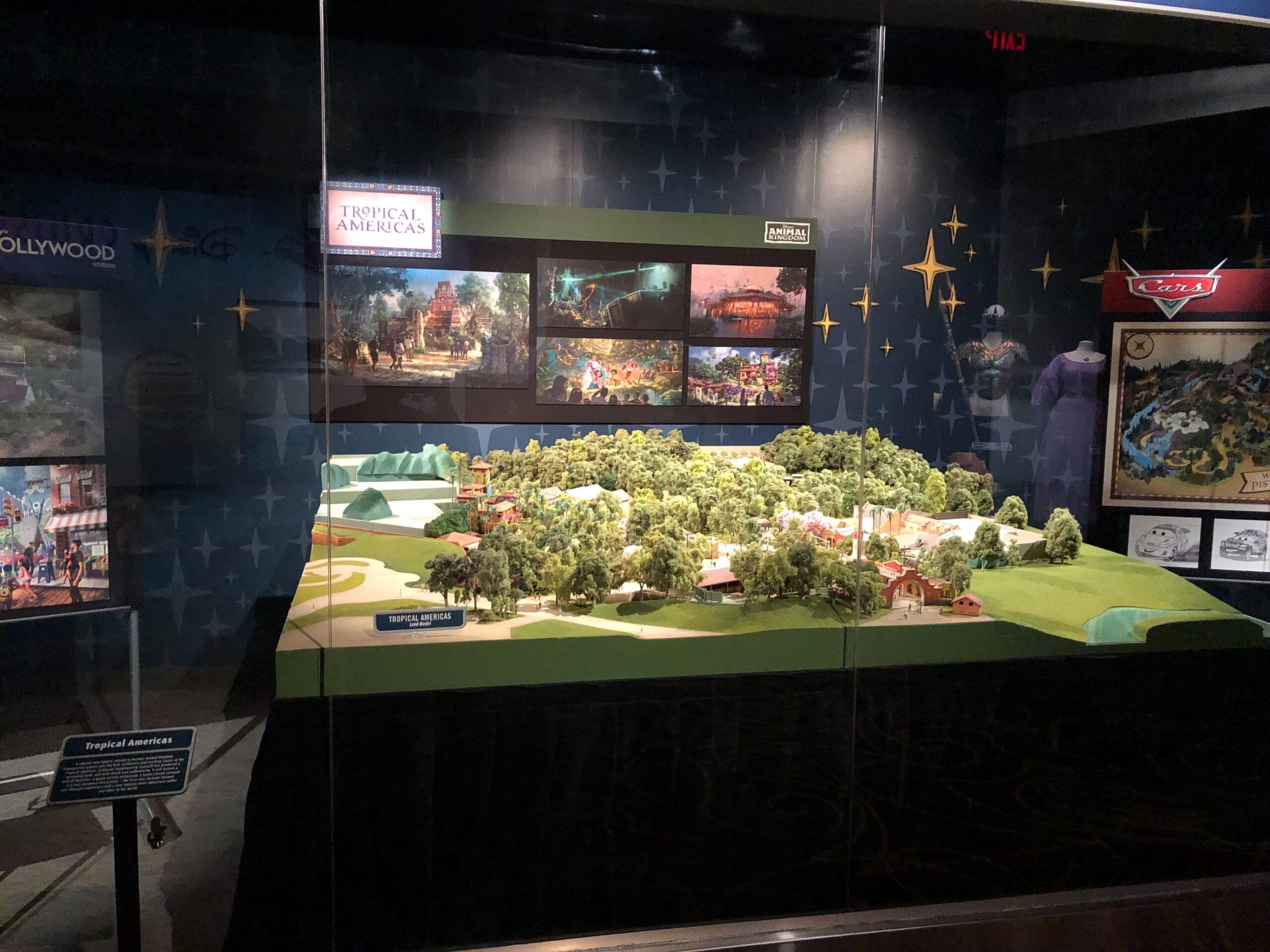 A display case features a scale model of Animal Kingdom’s Tropical Americas, with lush trees and structures—no castle present.