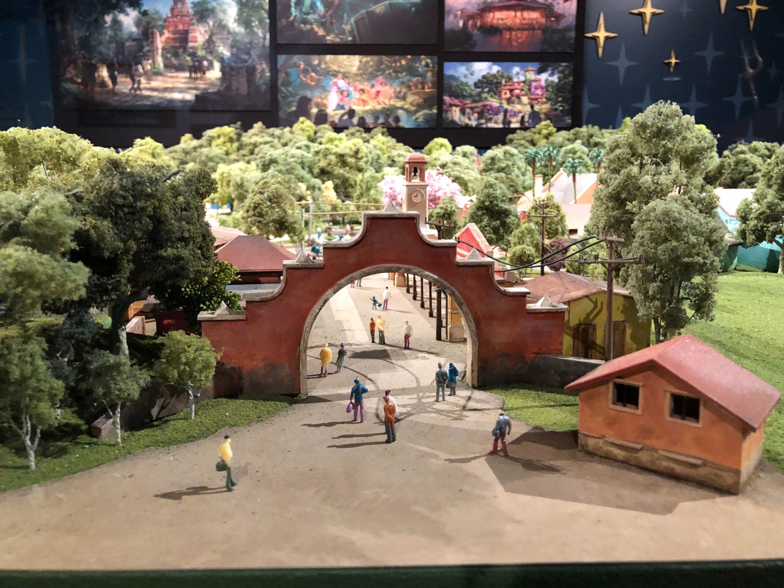 A detailed model of a Disney park entrance with a red archway, trees, Cars Land elements, and tiny figures like at Disneyland gates.