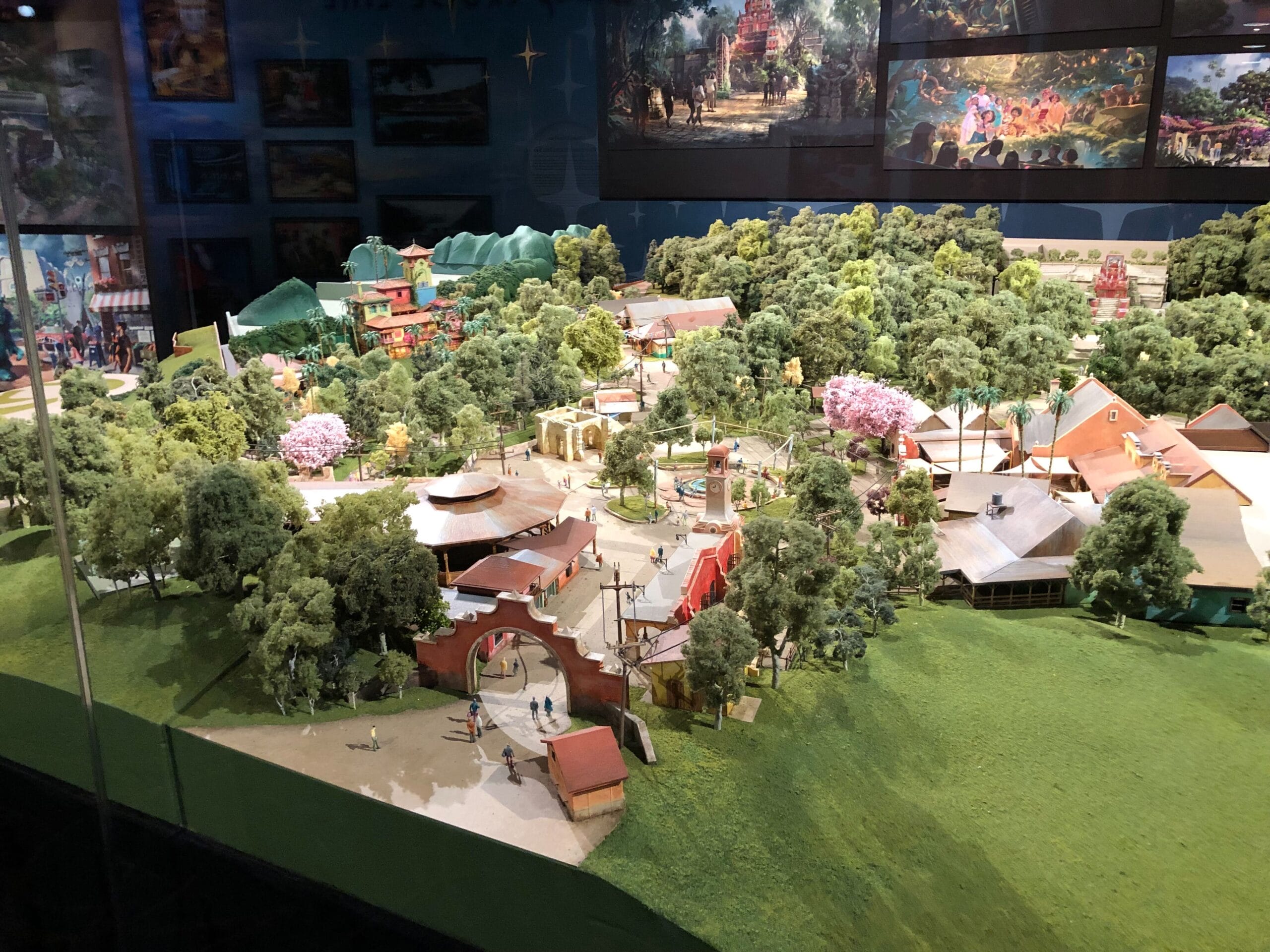 A detailed Cars Land miniature model featuring trees, paths, and buildings on display indoors at a Disney park, no castle present.