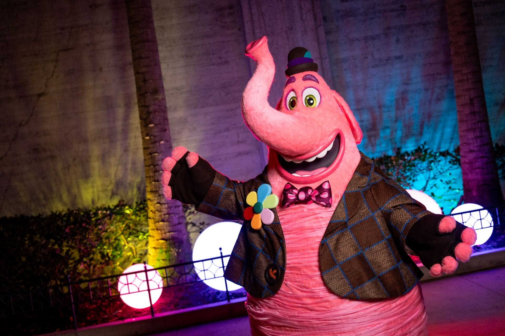 A person as Bing Bong in a plaid jacket poses with open arms in front of vibrant Disney Jollywood Nights lights, no castle visible.