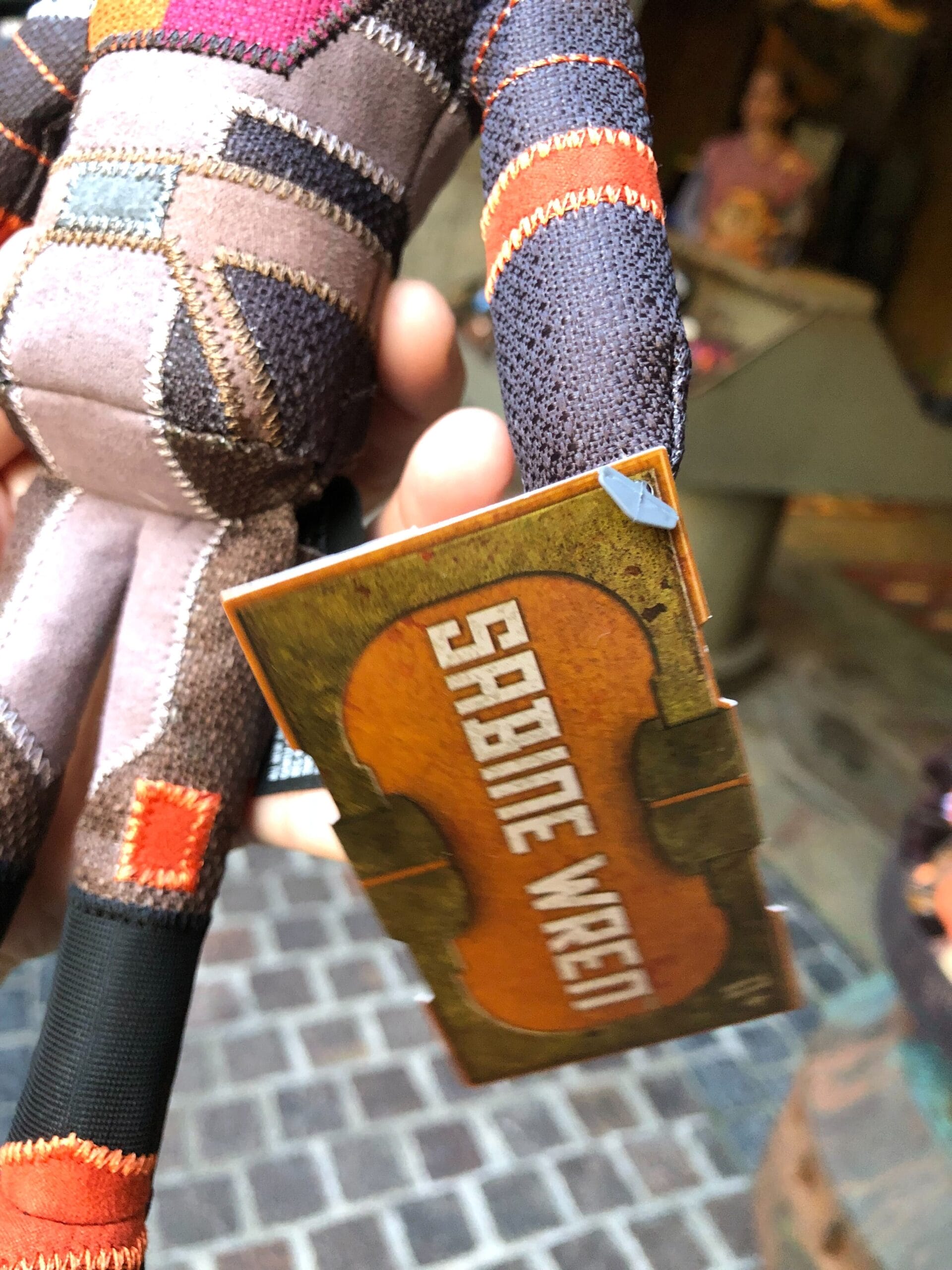 A hand holds a Sabine Wren plush with a tag at Star Wars Galaxy’s Edge, one of Disney Parks’ immersive themed lands—not a castle.