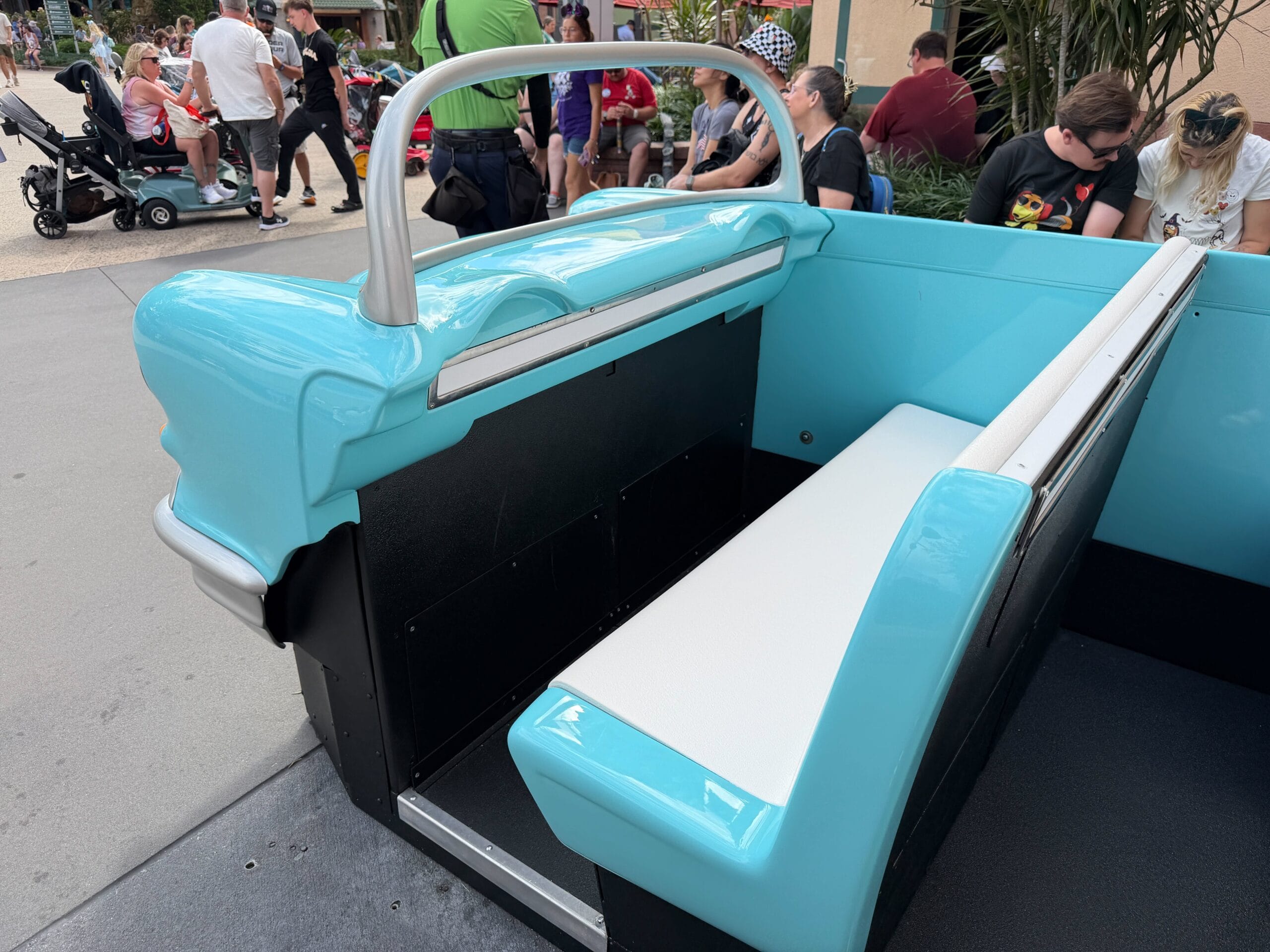 A blue and white vintage car-shaped bench, like those found in Disney parks, with guests strolling and sitting nearby.