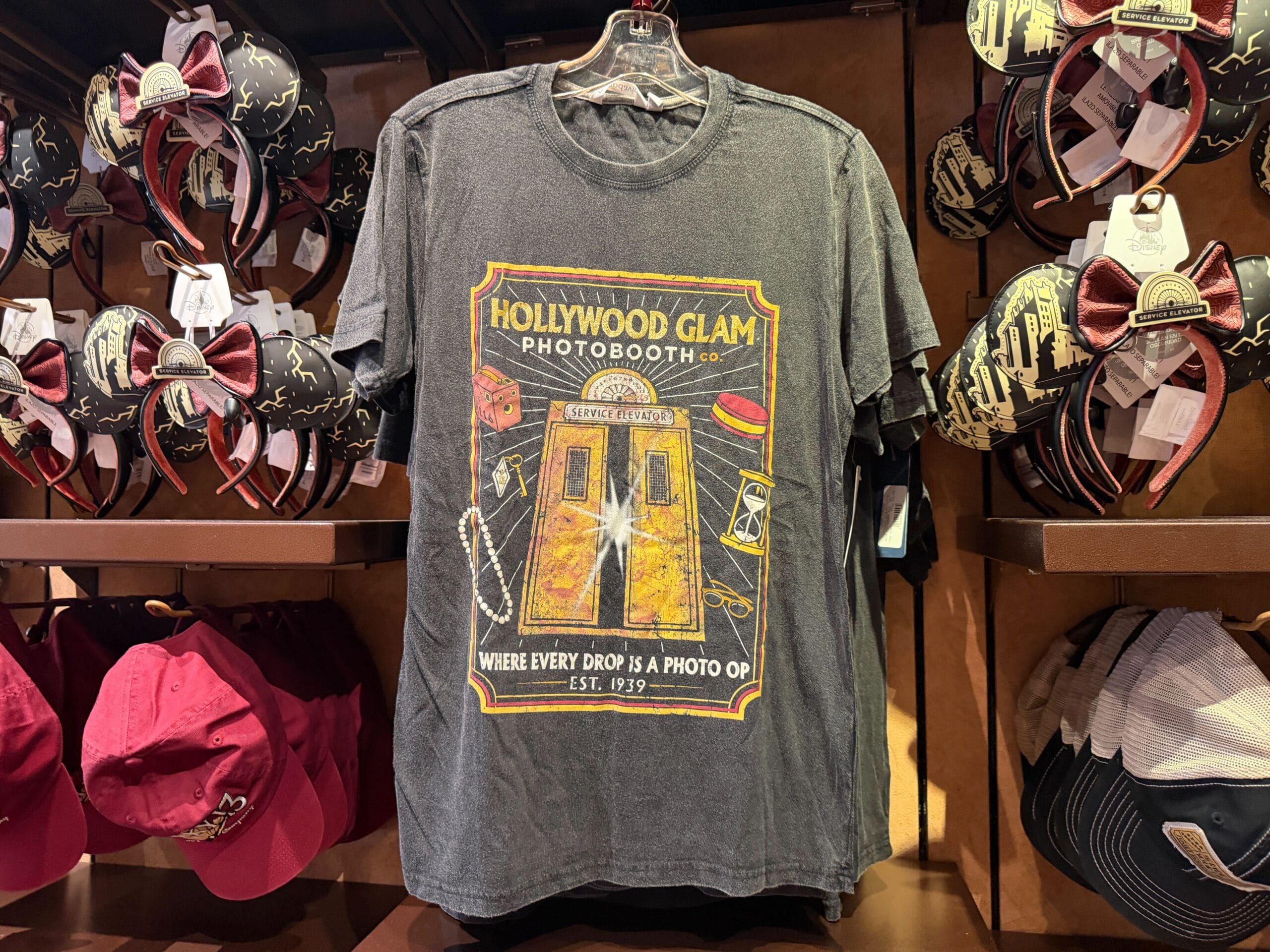Gray t-shirt with retro Hollywood photobooth print, displayed among hats and Minnie Mouse ears, reminiscent of Disney Park shops.