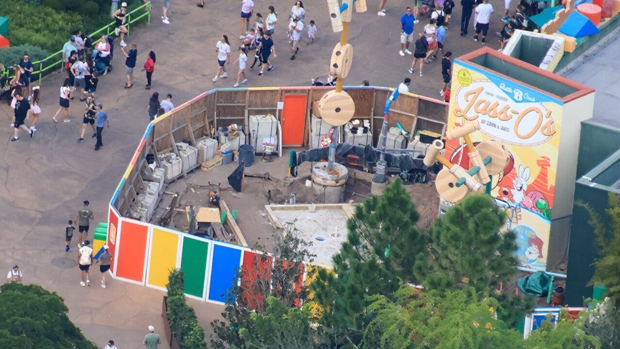 Aerial view of Toy Story Land at a Disney park, vibrant crowds, colorful decor, and Food Kiosk construction, no castle in sight.