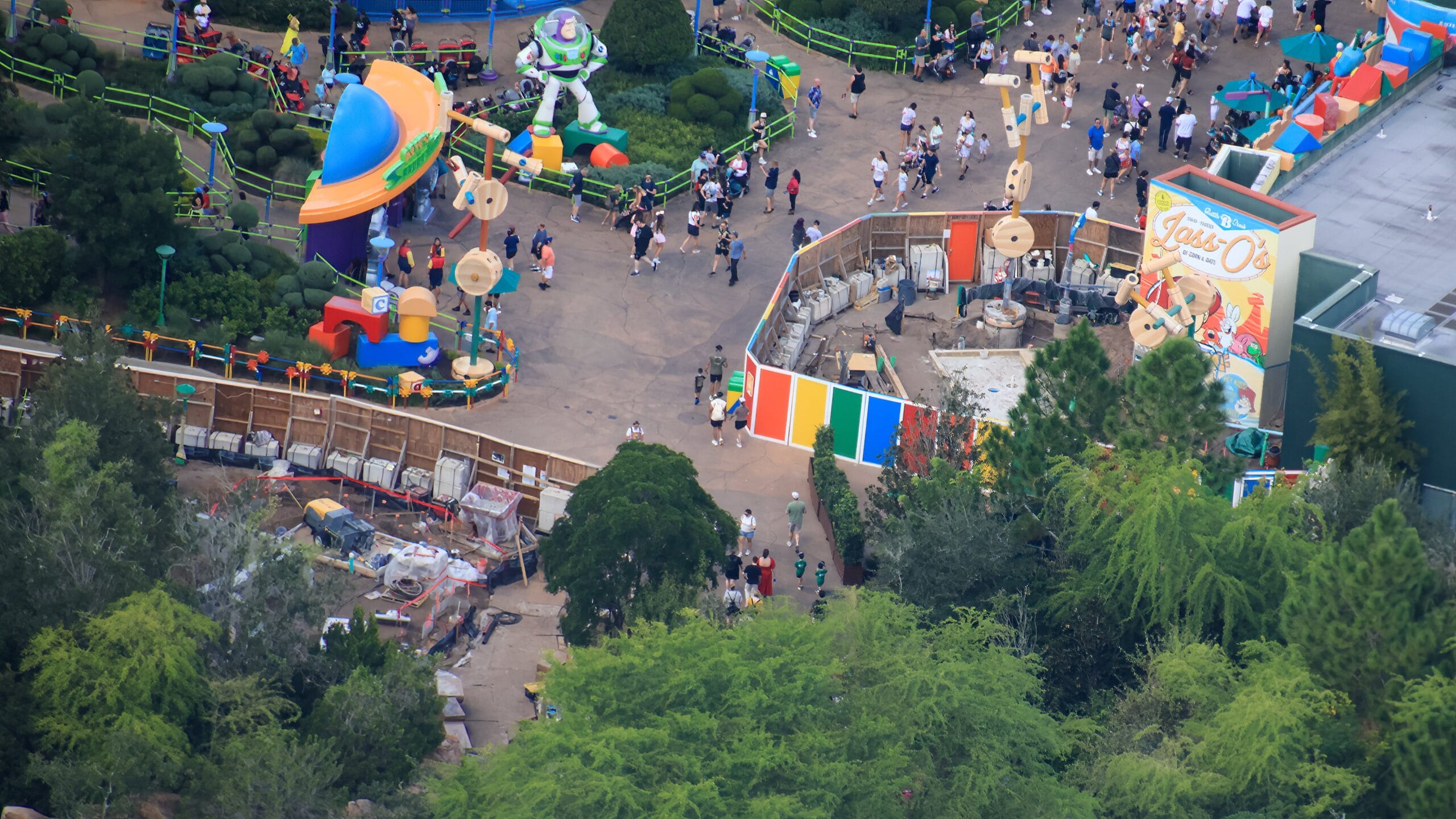 Aerial view of Toy Story Land at a Disney park, vibrant crowds, colorful decor, and Food Kiosk construction, no castle in sight.