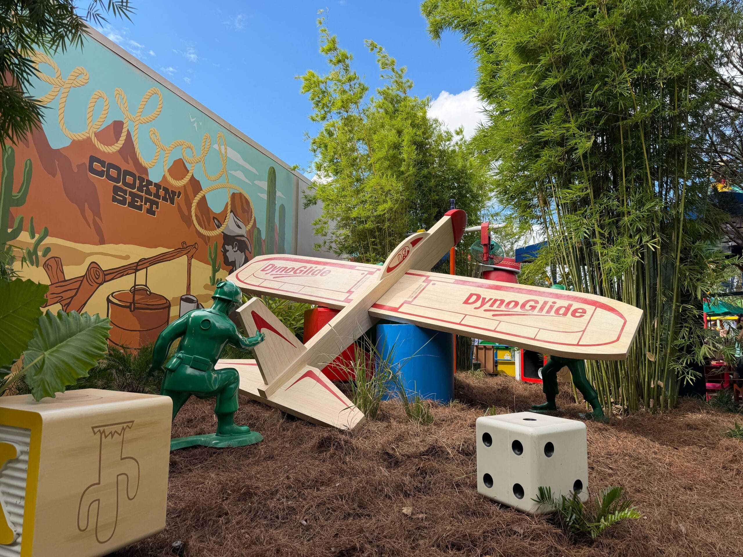 Green toy soldiers arrange a wooden toy airplane with a six-sided die and wooden block nearby, outside Toy Story Mania in Disney's Hollywood Studios.