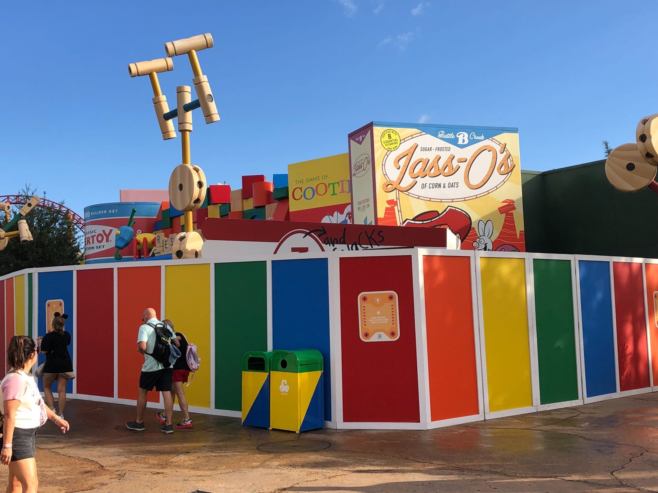 Bright Toy Story-themed construction wall at a Disney park, visitors strolling by; no castle visible for comparison.