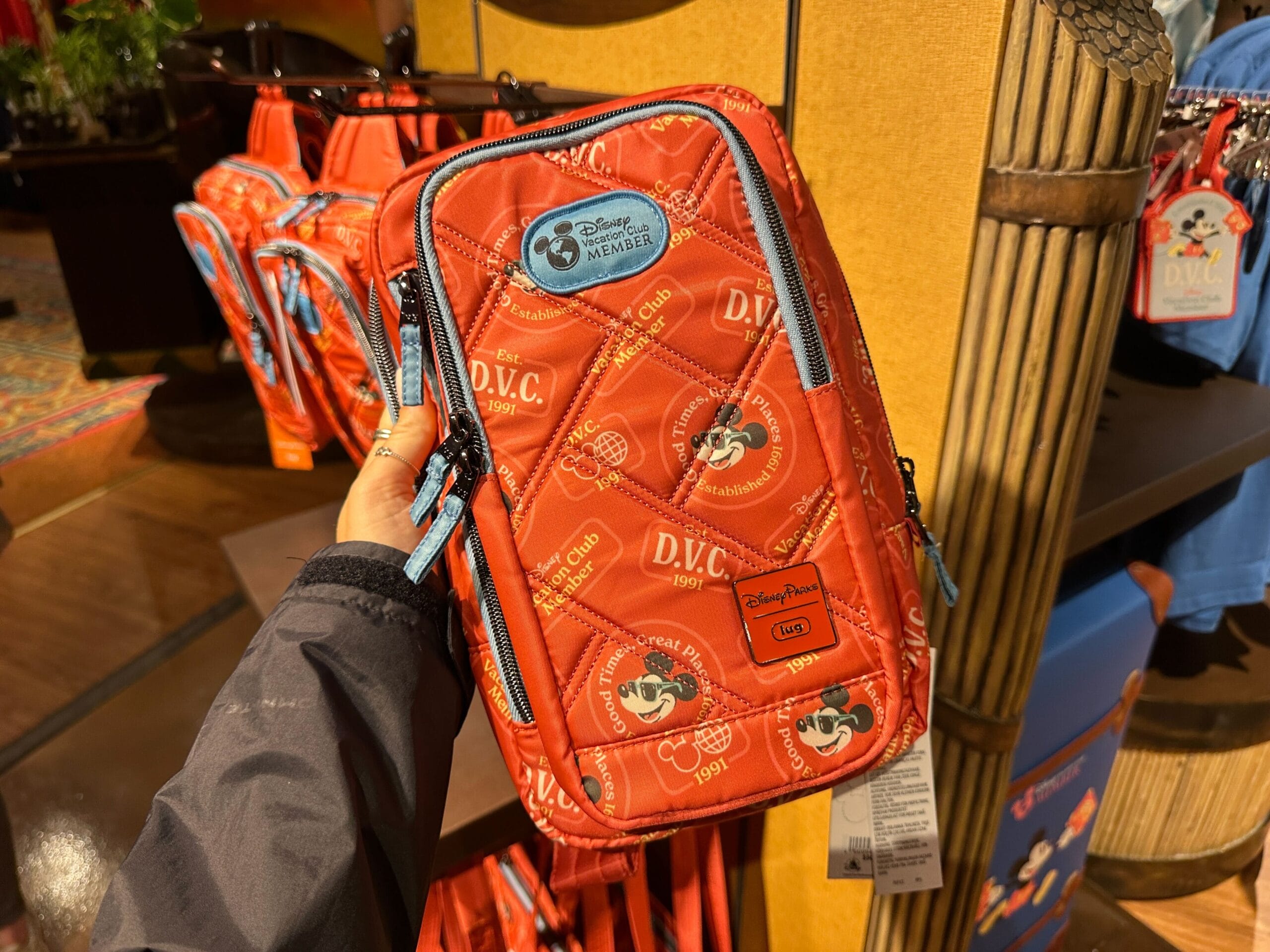 A hand holds DVC Member Merch—a red bag with Mickey—at Disney's Grand Floridian Resort store display.