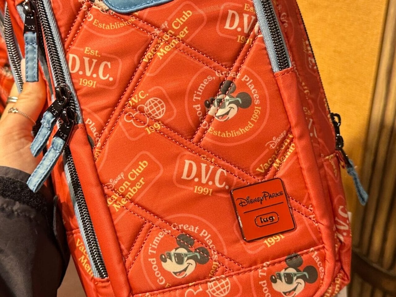 A hand holds a red Lug Bag with Mickey DVC Member logos at a Disney World store display.