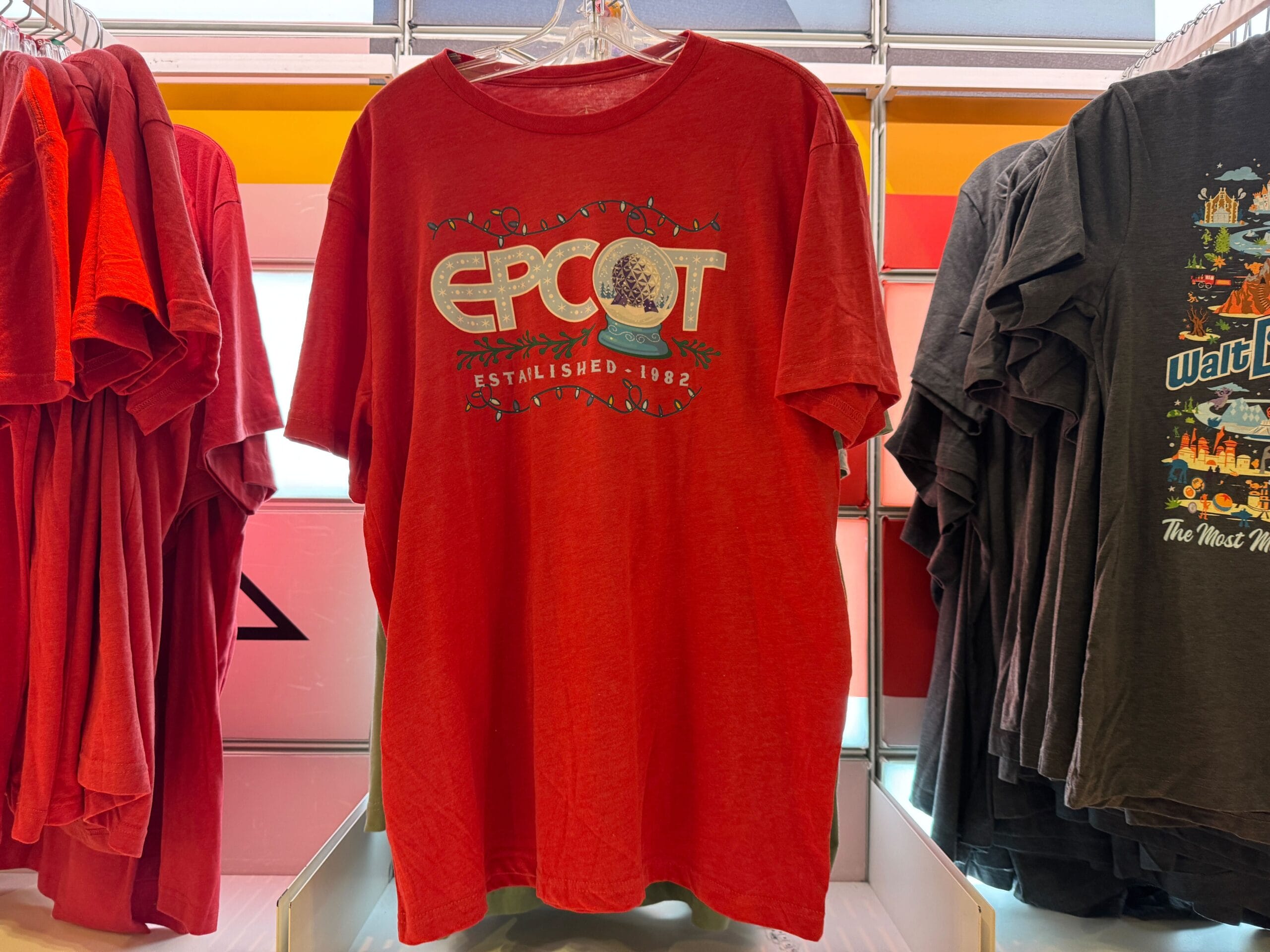 Red T-shirt featuring "EPCOT Established 1982" with a Spaceship Earth graphic, on display rack; nod to Walt Disney World’s Epcot.