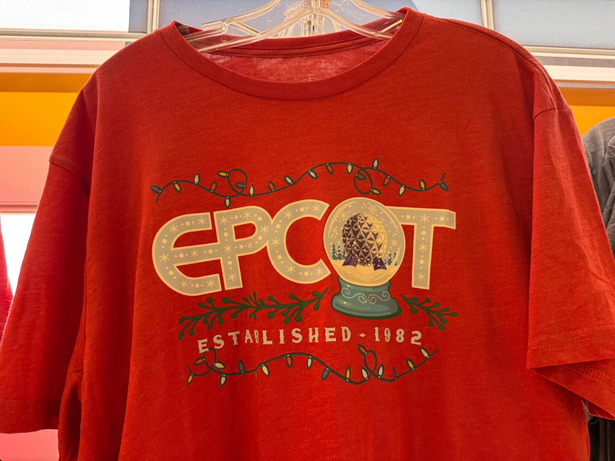 Red EPCOT shirt with "Established 1982" and a snow globe of Spaceship Earth covered in festive holiday lights, classic Epcot style.