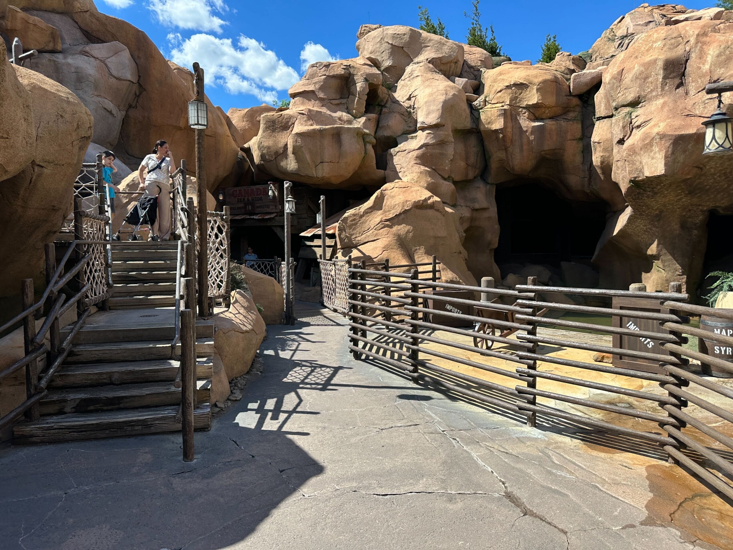 Guests stand on a wooden deck by rocky formations under a clear sky, similar to areas in Disneyland’s Frontierland.