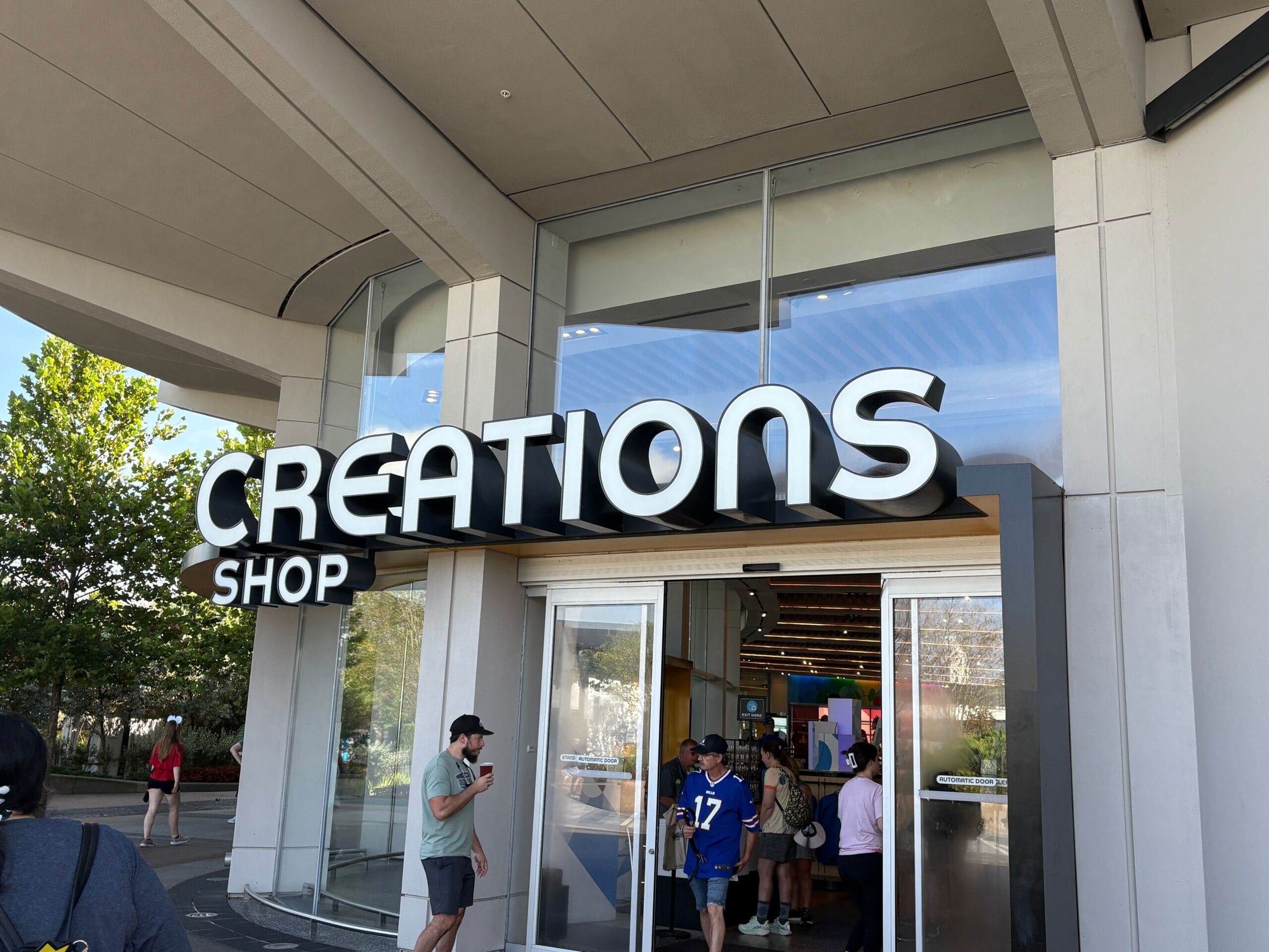 People entering and exiting a store with a large "Creations Shop" sign above the entrance in EPCOT.