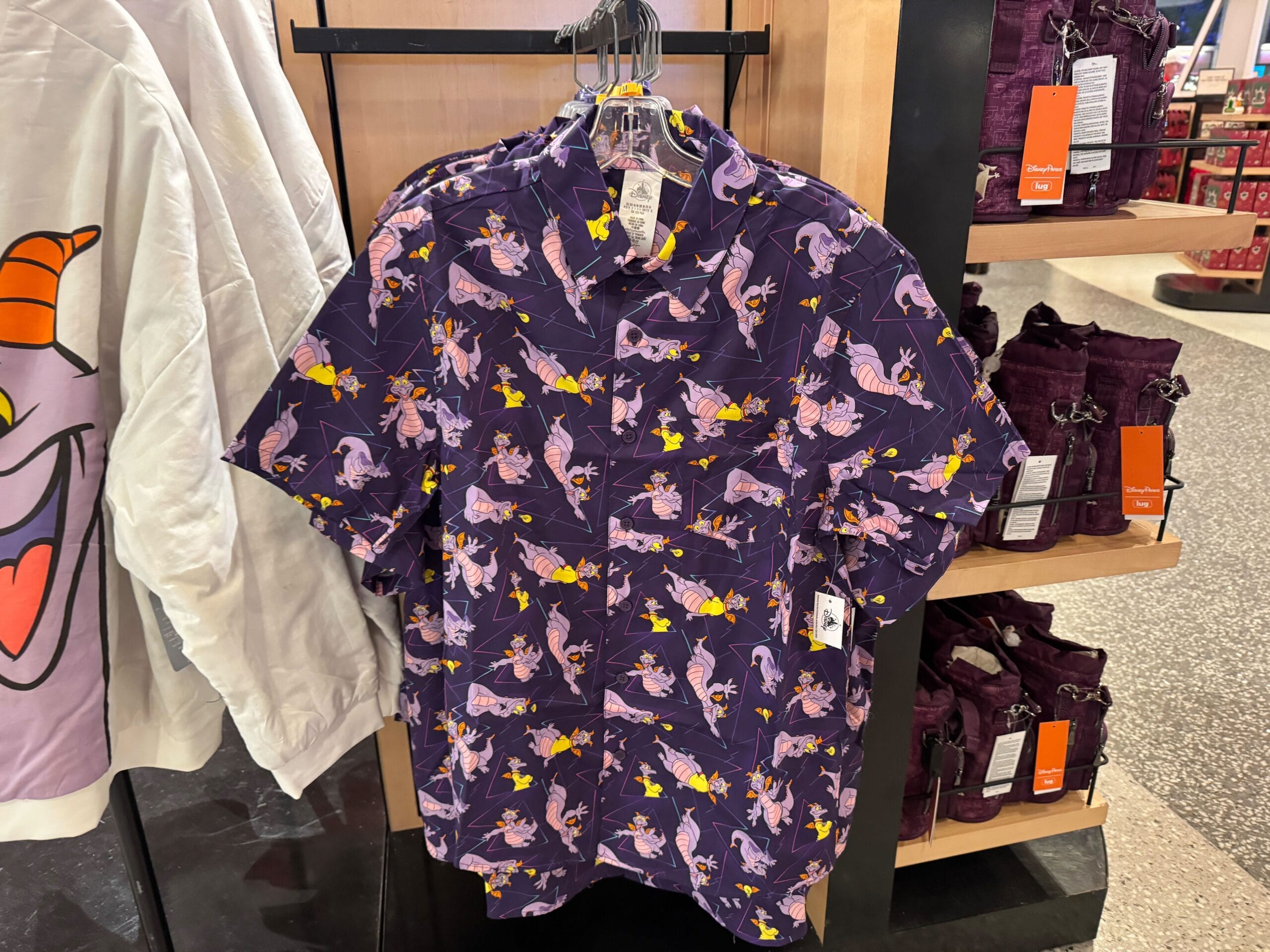 Purple button-up shirt featuring whimsical dragon and yellow stars, hanging in a Disney Parks shop, reminiscent of Figment merch.