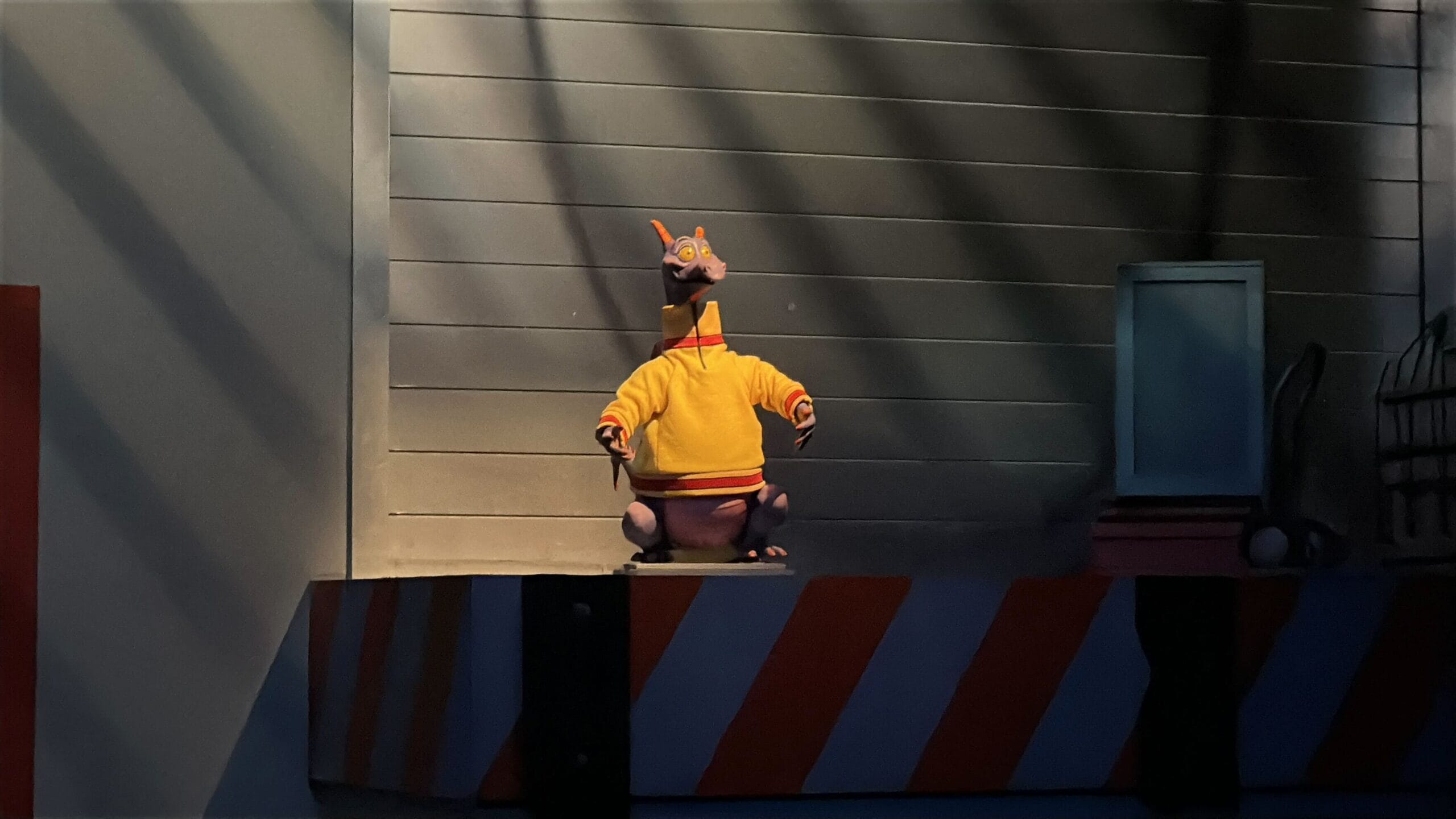 A purple dragon inspired by the 1983 Epcot Figment figure stands on a striped platform under dramatic, Disney-style lighting.