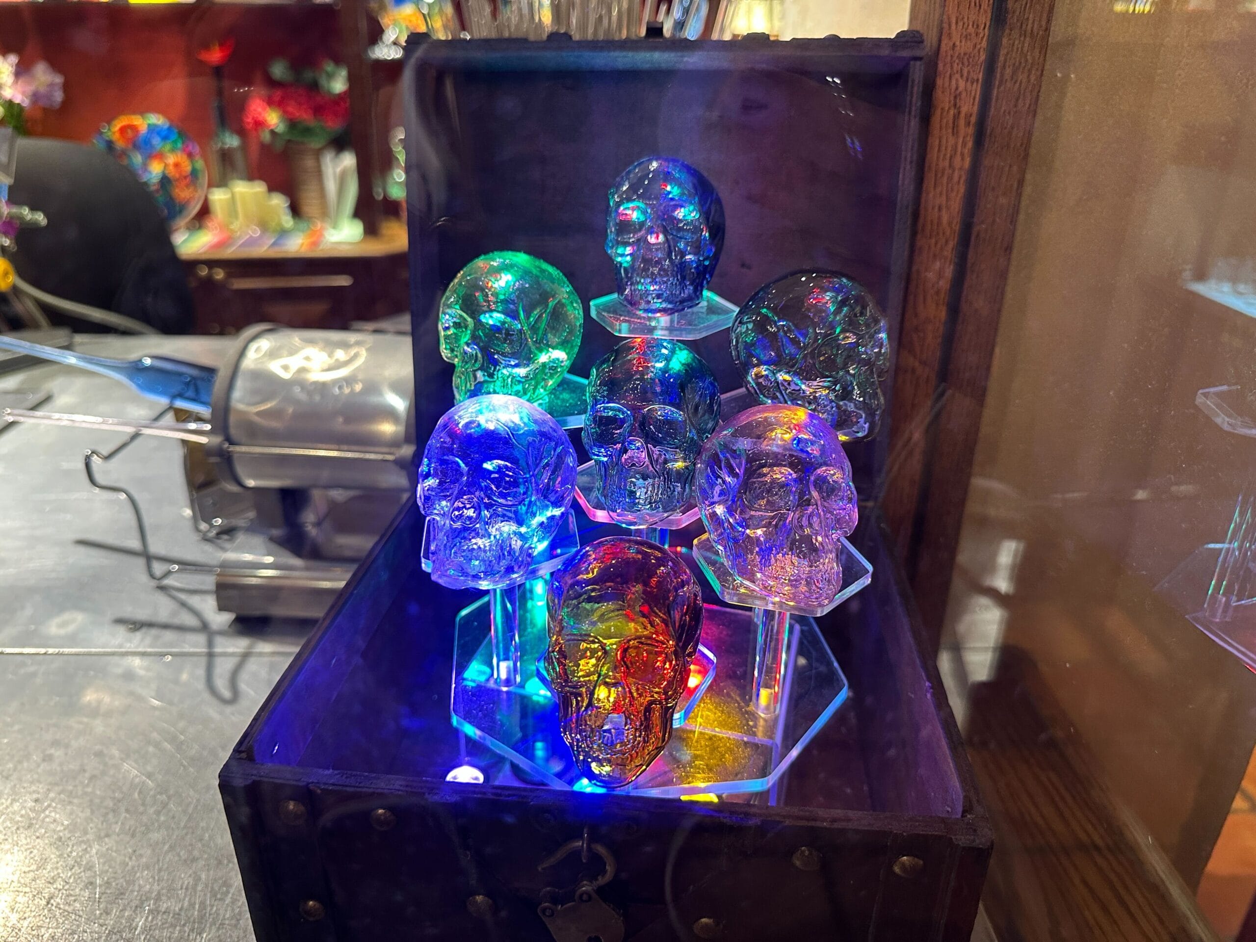 Seven glass skulls, glowing with vibrant lights in a dark shop display, like the Haunted Mansion curios sold at Disney parks.