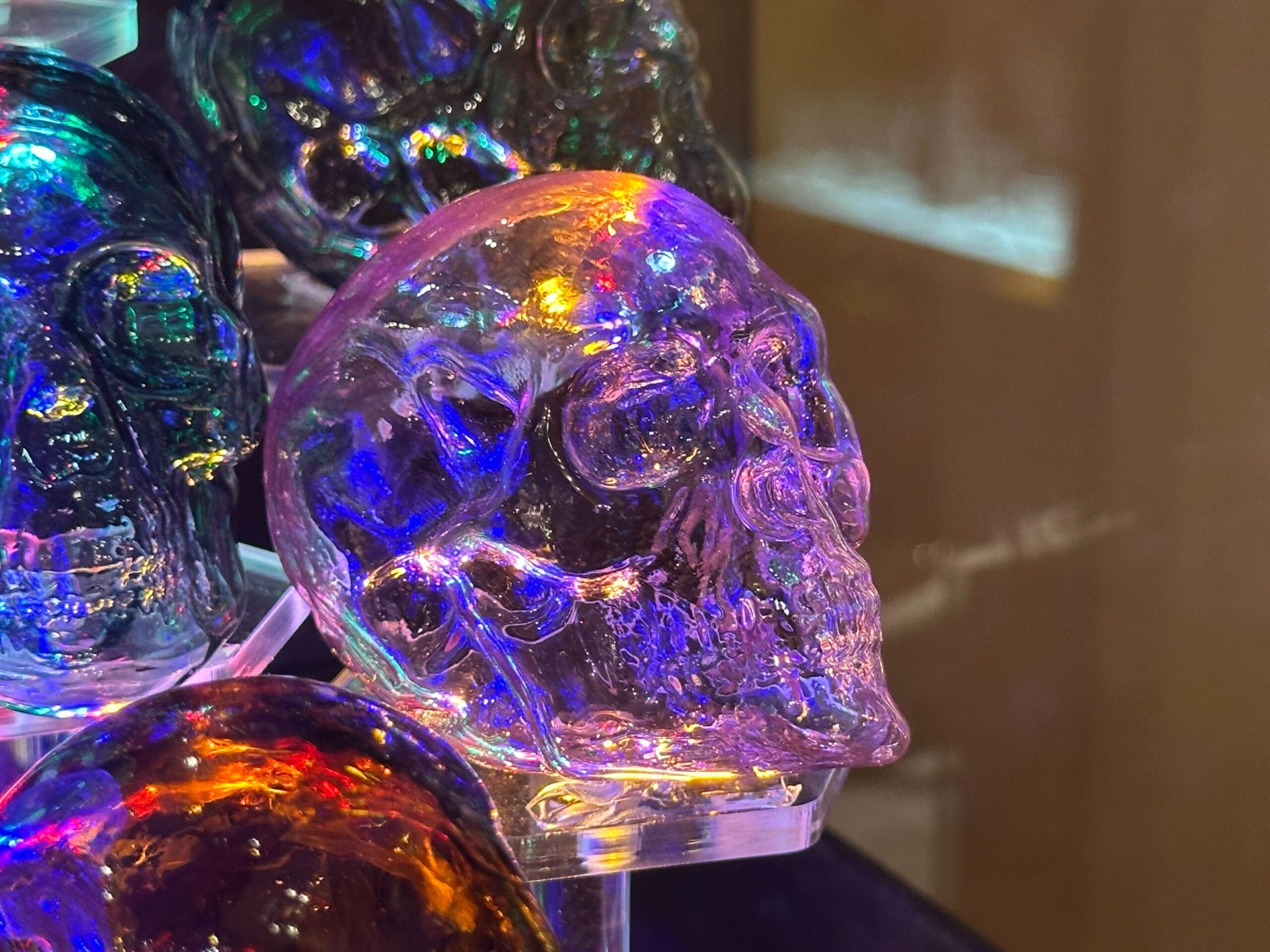 A glass skull lit with vibrant purple, blue, and orange hues, echoing the colorful nighttime lights seen in Disney park displays.