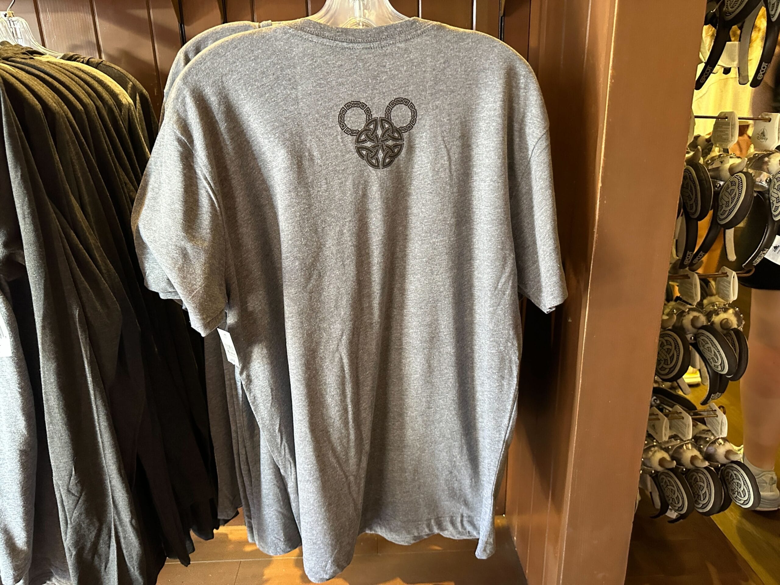 Back of gray t-shirt on a rack, featuring a small black Nordic-inspired Mickey Mouse head design near the neck.