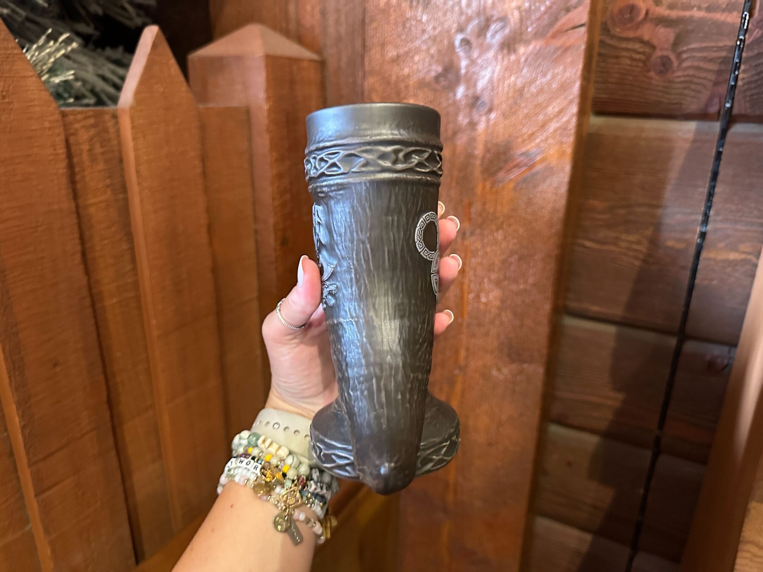 Side view of a brown ceramic drinking horn-shaped mug showing a knotwork pattern sculpted around the top and base.