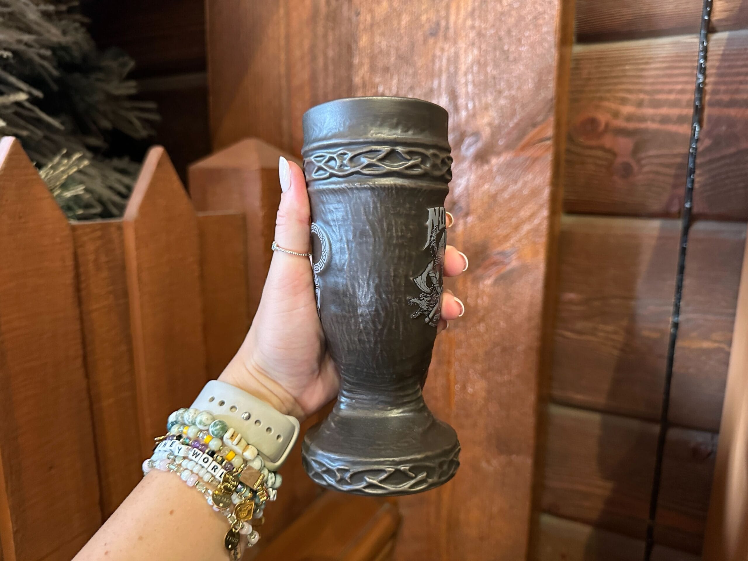 Side view of a brown ceramic drinking horn-shaped mug showing a knotwork pattern sculpted around the top and base.