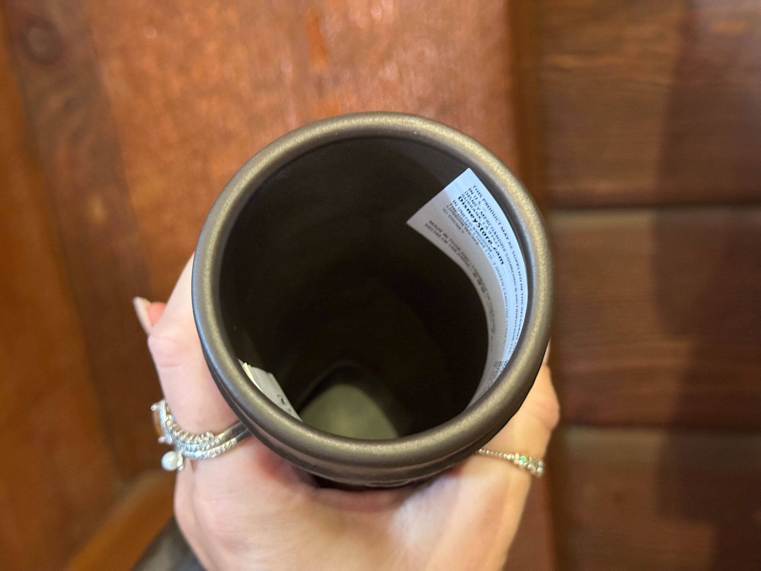 A hand holds a dark brown ceramic cup with a visible label inside.