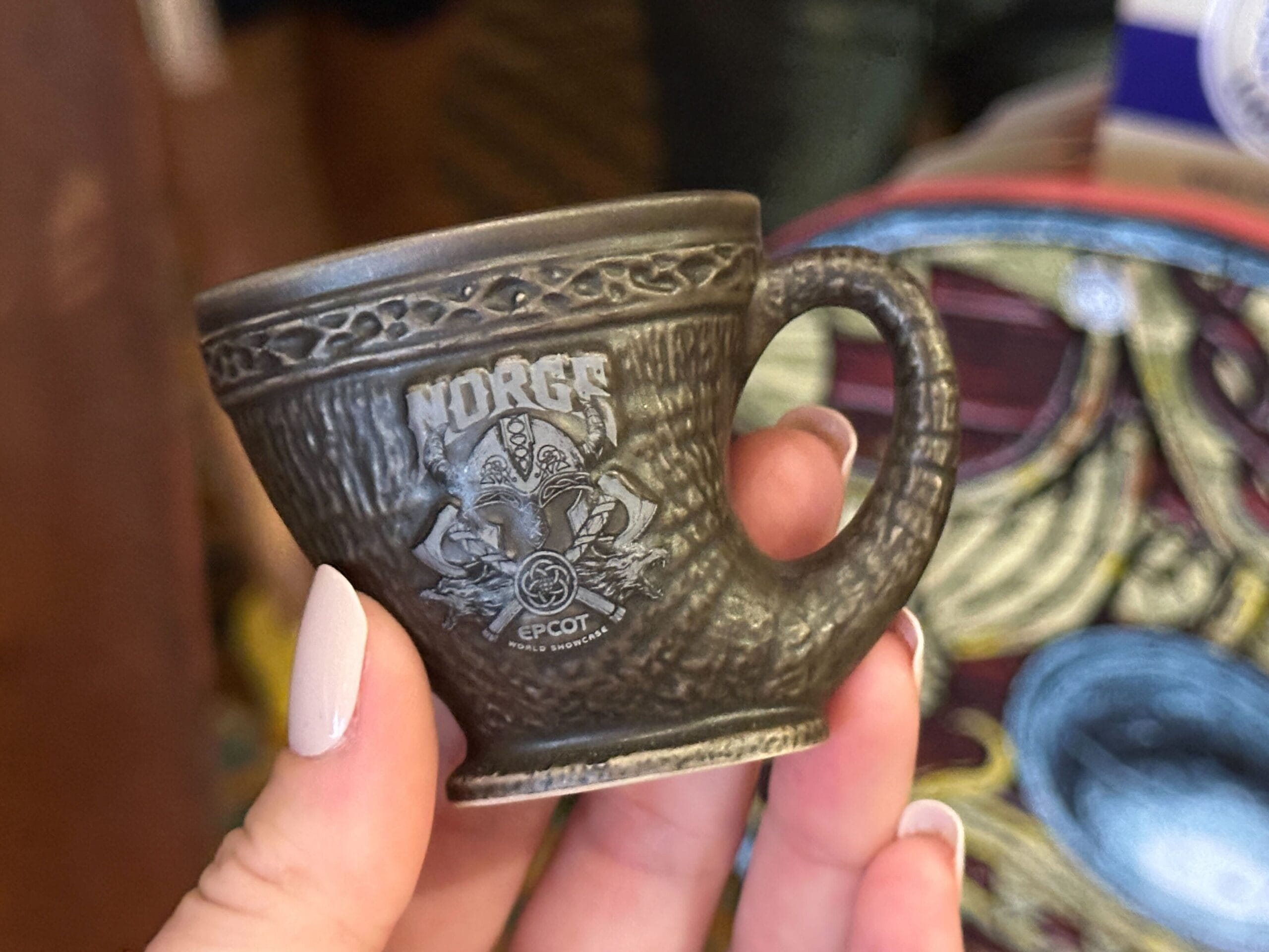 A hand holds a small brown horn-shaped "Norge EPCOT World Showcase" ceramic shot glass with a Viking helmet design.