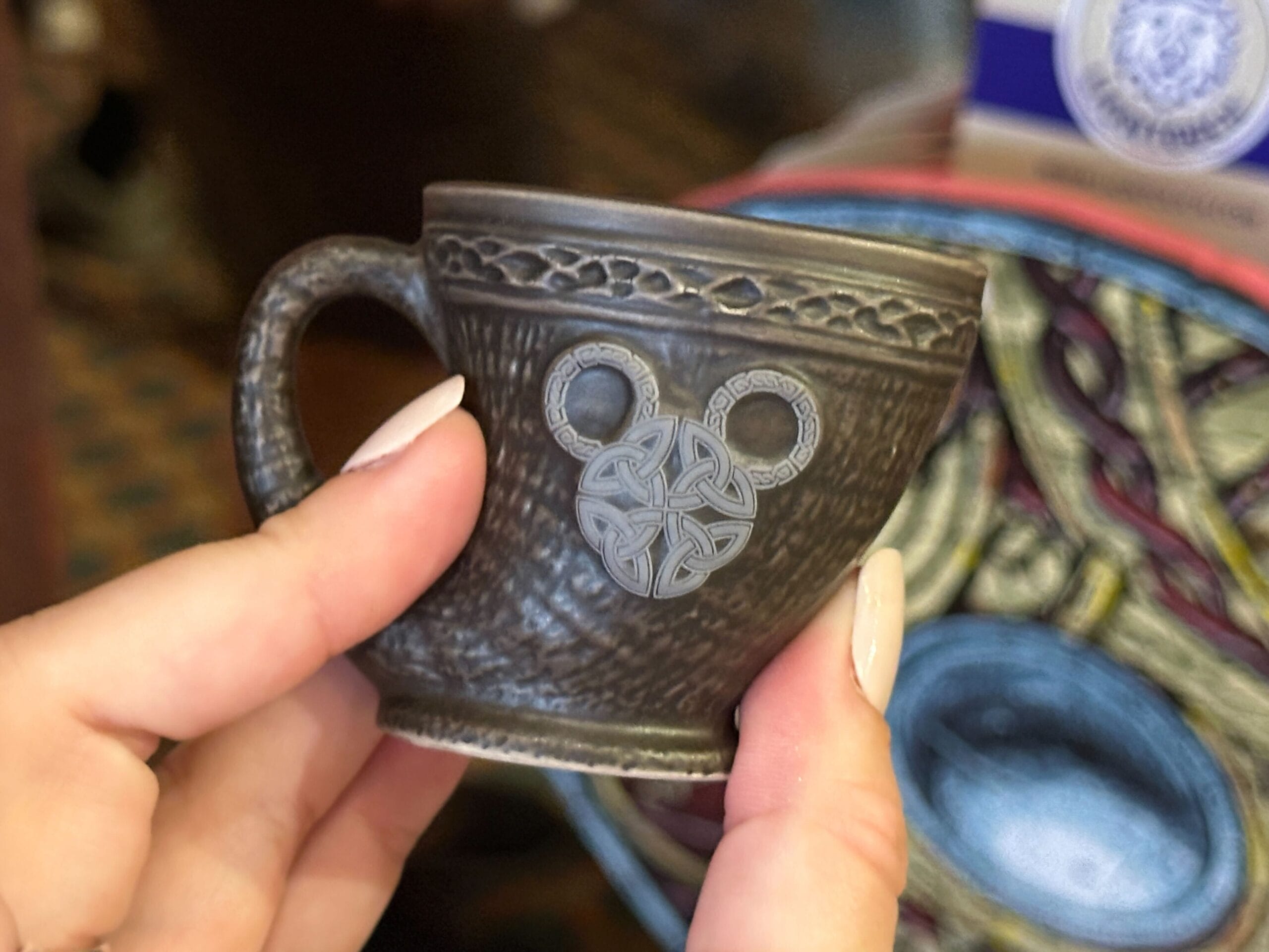 A hand holds a small brown horn-shaped ceramic shot glass with a Nordic-inspired Mickey head design.