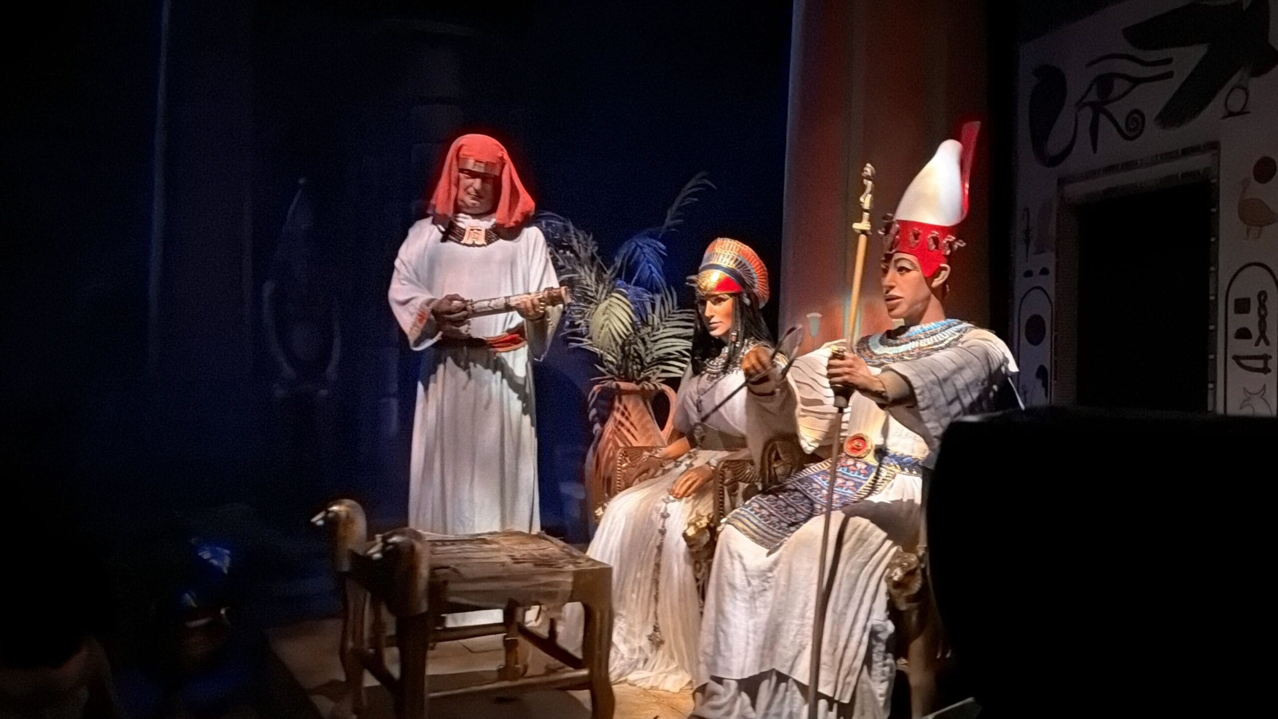Three people dressed as ancient Egyptian royalty discuss a scroll, reminiscent of the storytelling in Spaceship Earth at EPCOT.