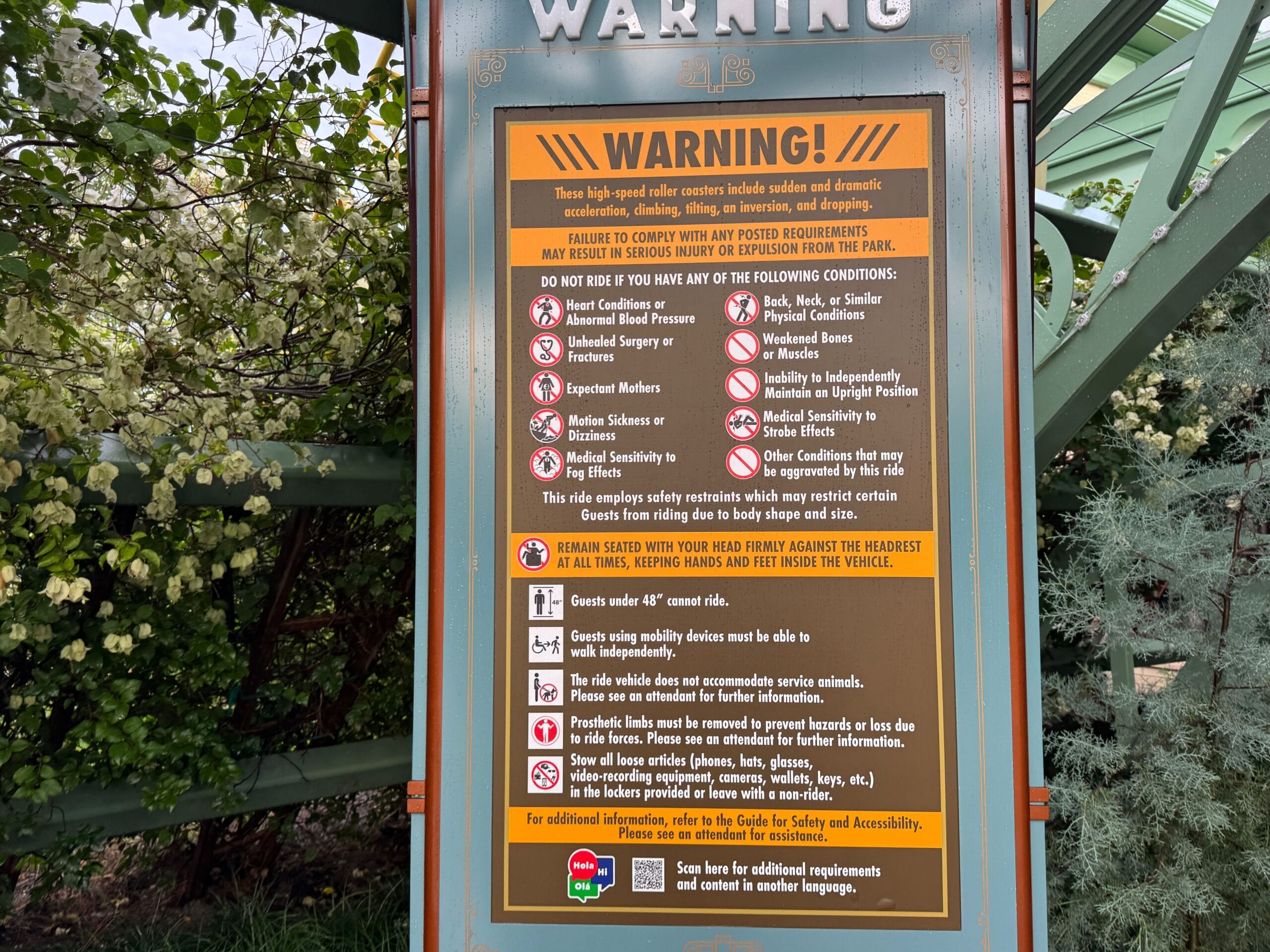 Warning sign at Epic Universe lists Stardust Racers safety rules, rider restrictions, and guest guidelines amid greenery.