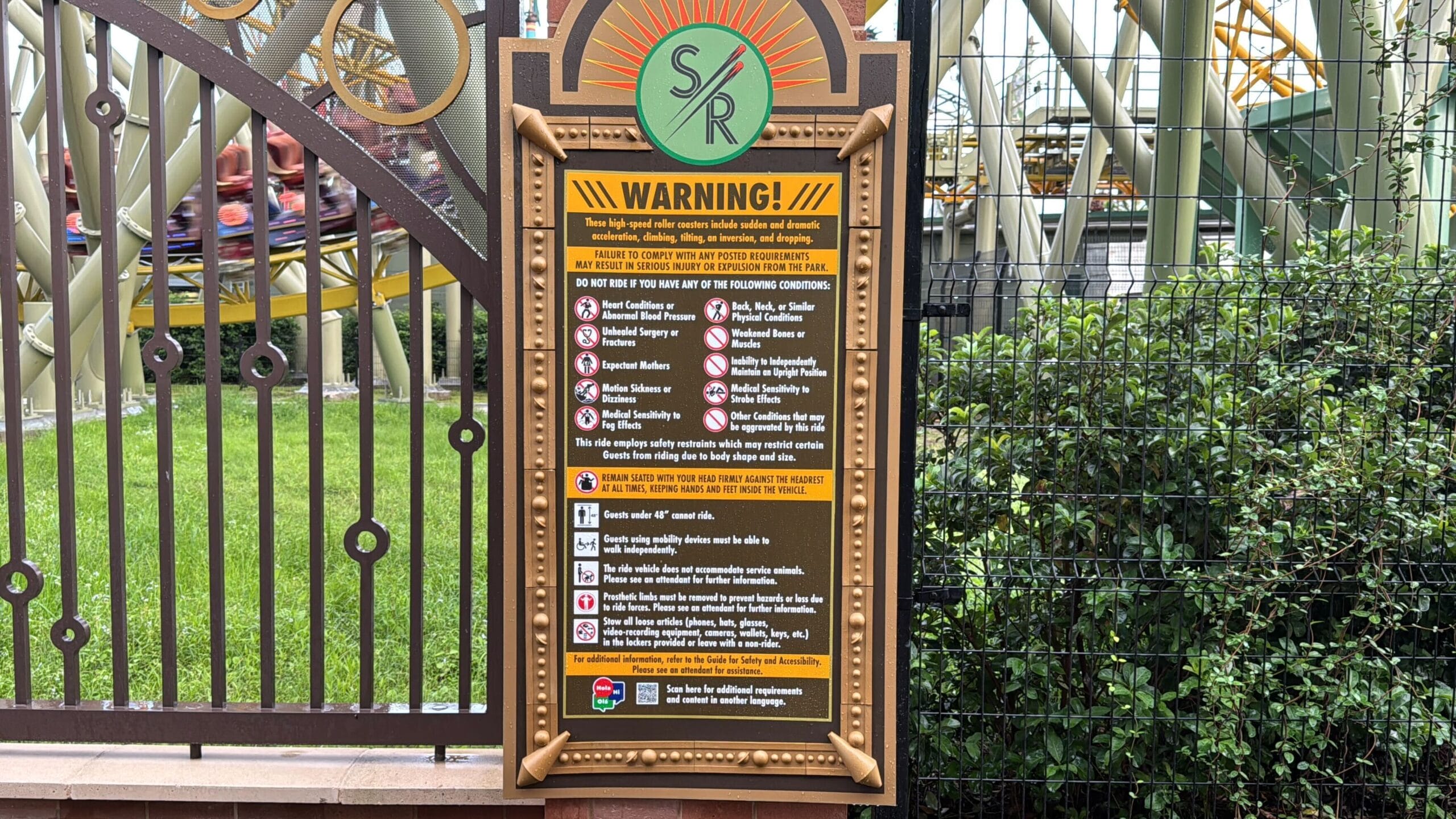 Warning sign at Stardust Racers roller coaster entrance lists safety rules, set by a fence and greenery for Epic Universe reopening.