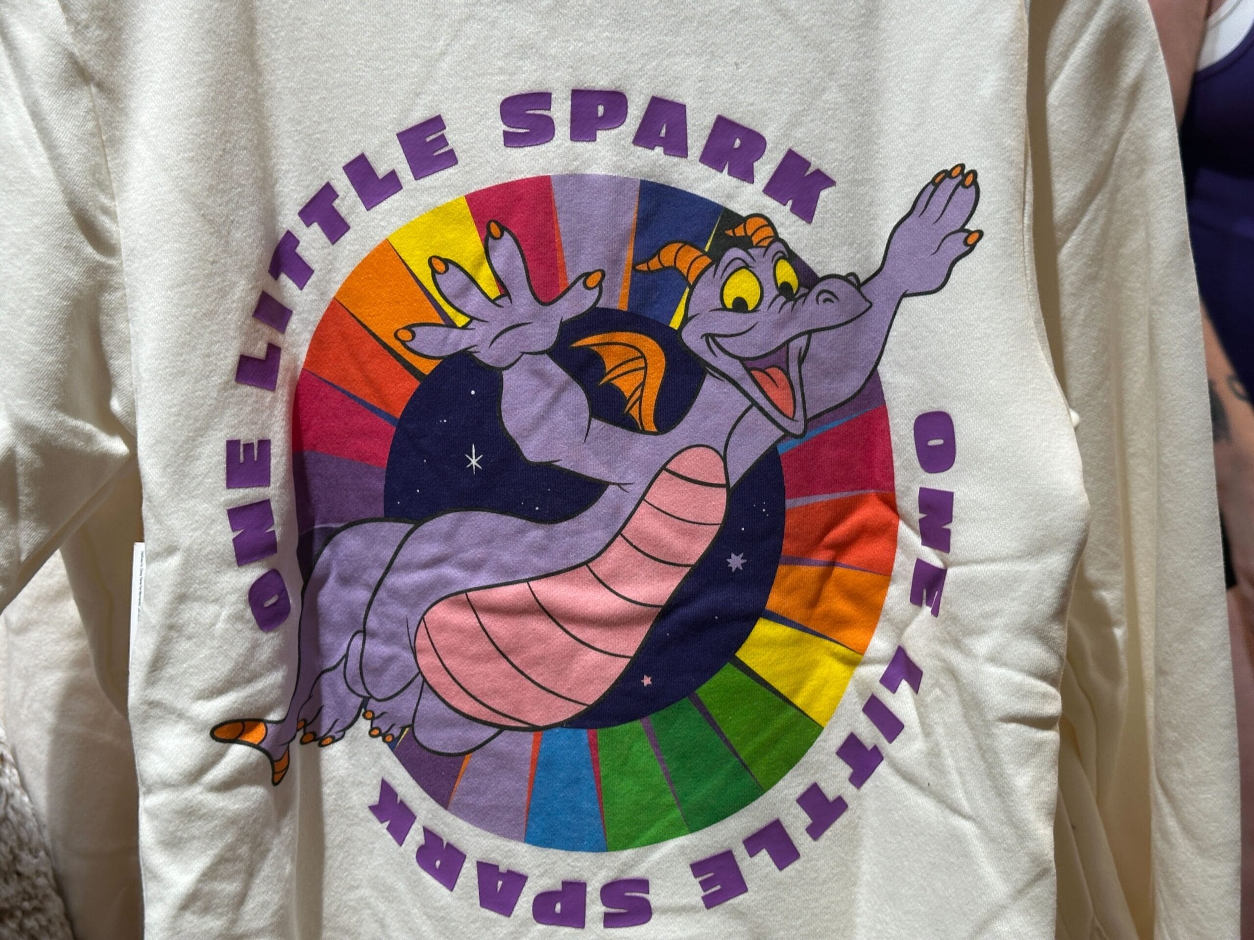 A shirt featuring EPCOT’s Figment the purple dragon inside a rainbow circle with “ONE LITTLE SPARK,” no castle imagery present.