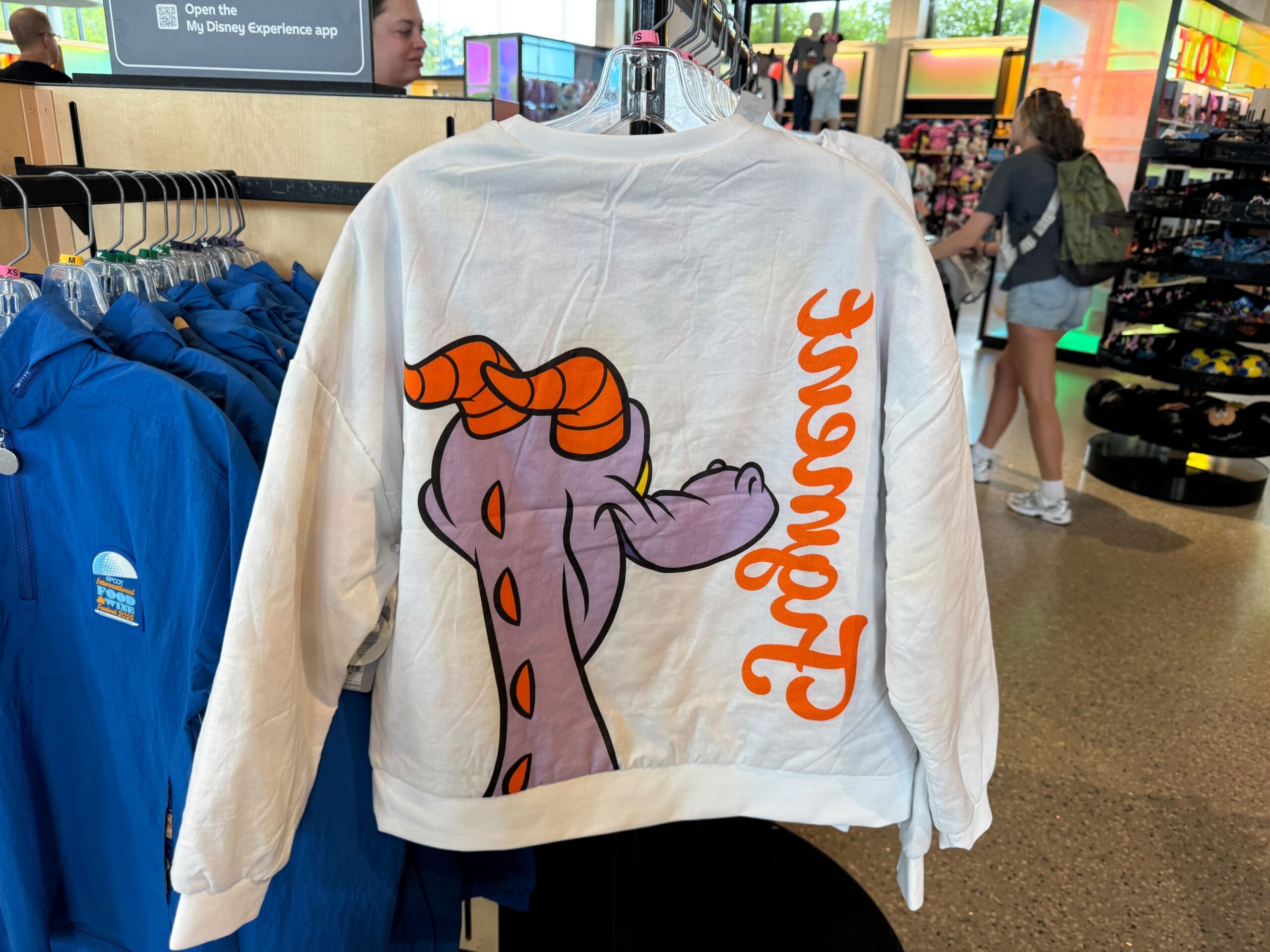 A white jacket with a cartoon dragon and orange "Figment" text, displayed in a retail store.